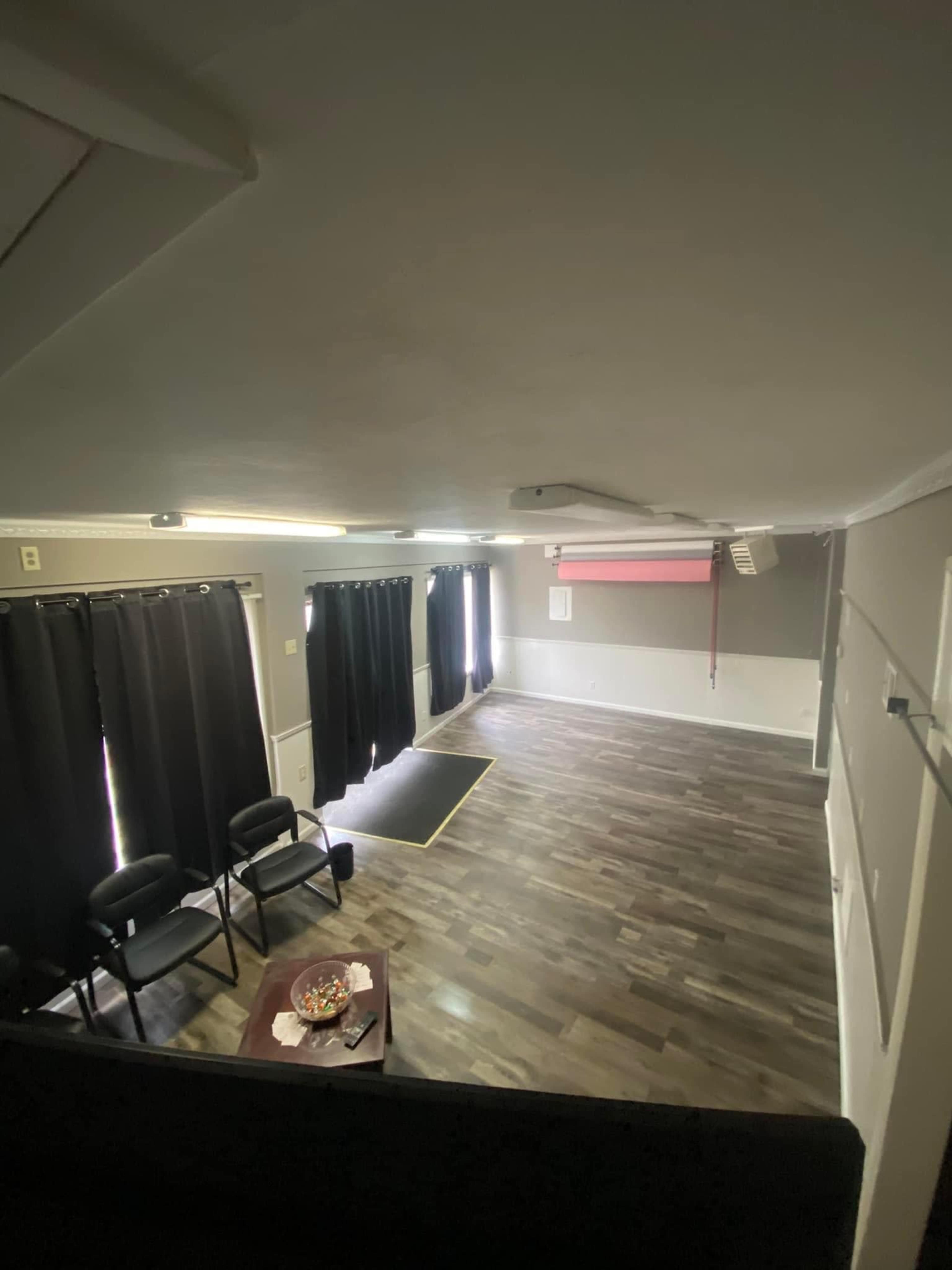 A spacious room with dark curtains, wooden flooring, and two chairs arranged around a low table.