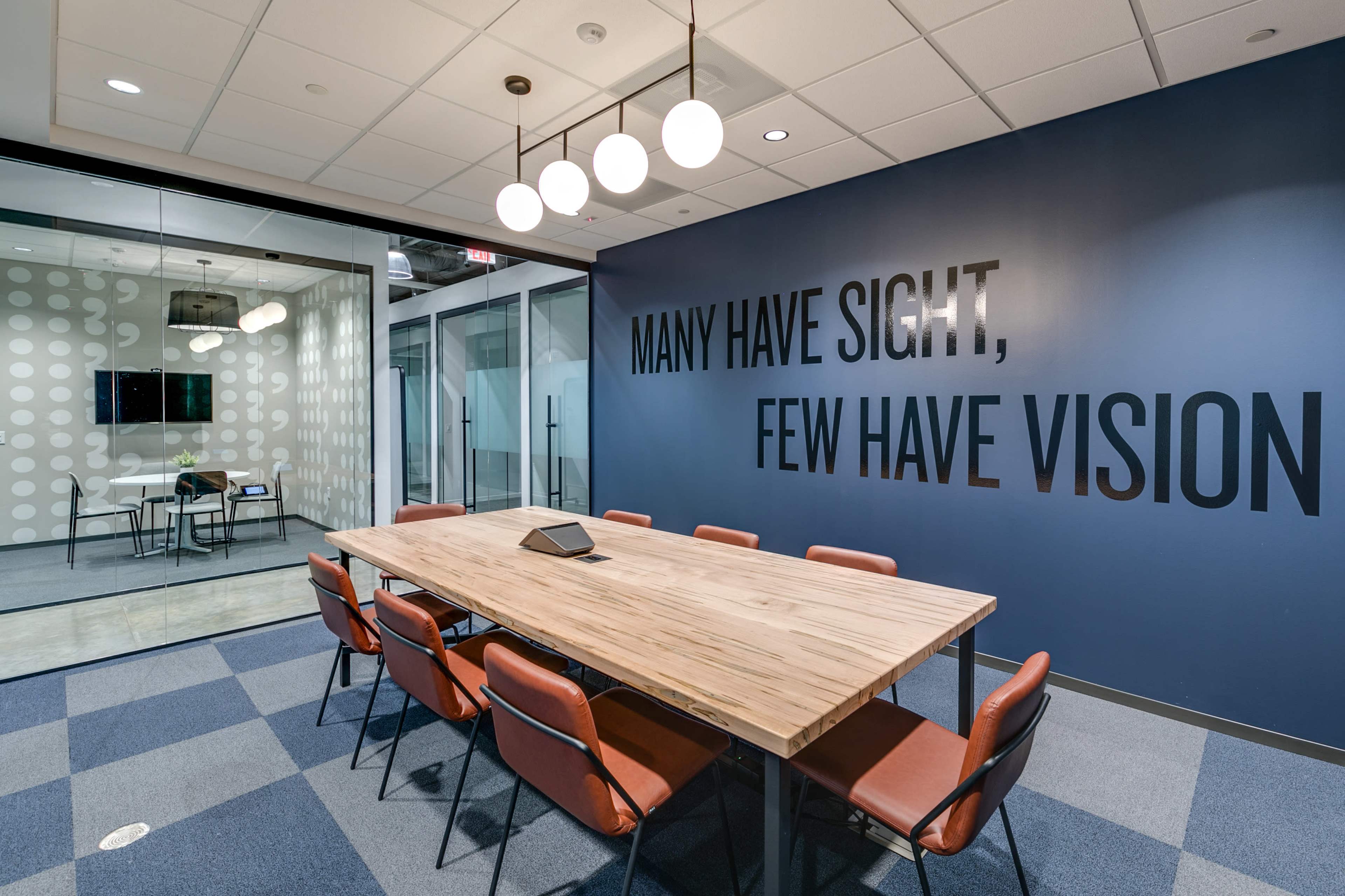 The image shows a modern conference room with a wooden table and eight chairs, featuring a dark blue wall that has the phrase "MANY HAVE SIGHT, FEW HAVE VISION" prominently displayed.