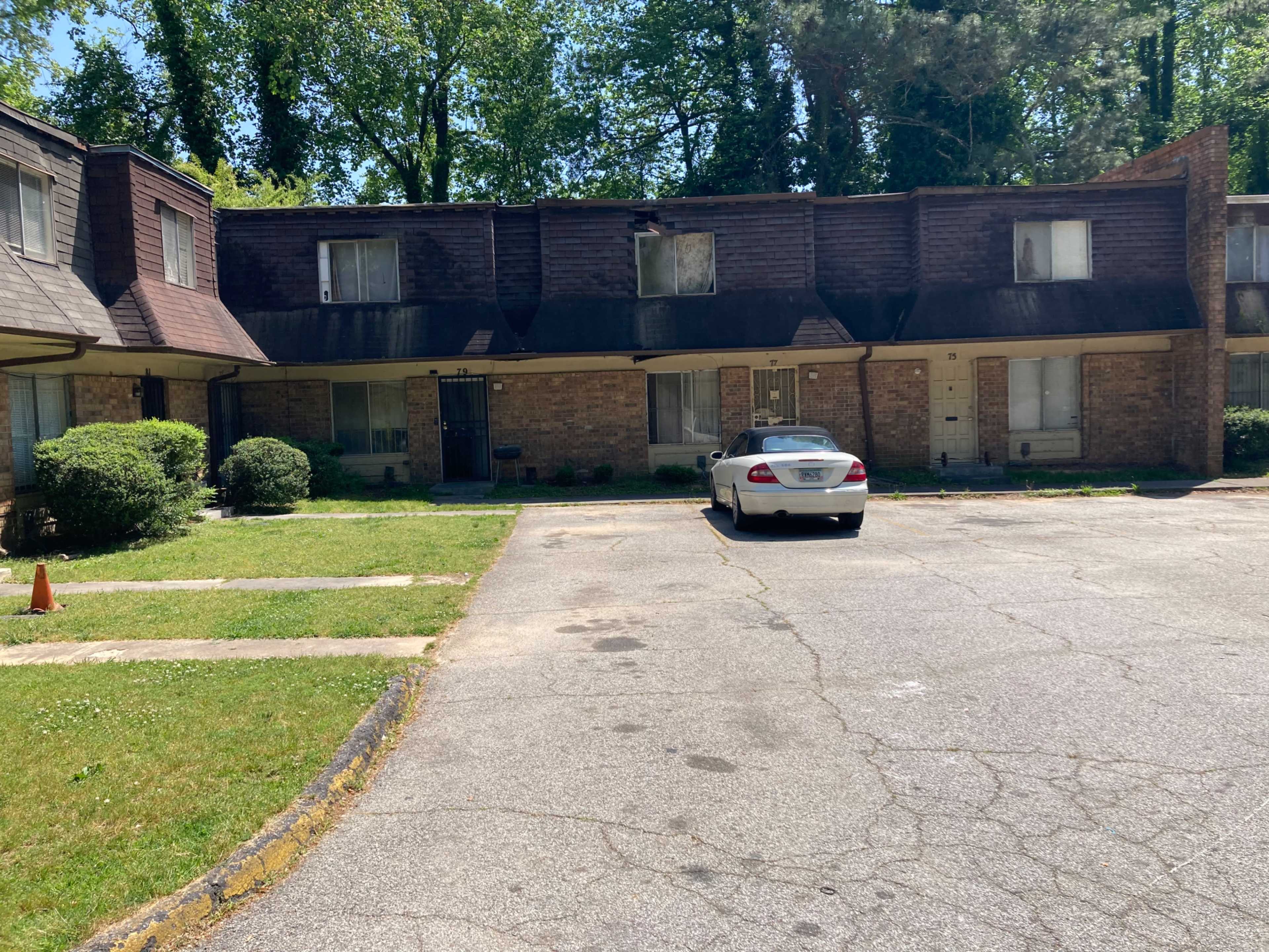 A multi-unit residential building with a gravel parking area, featuring a white car parked in front.