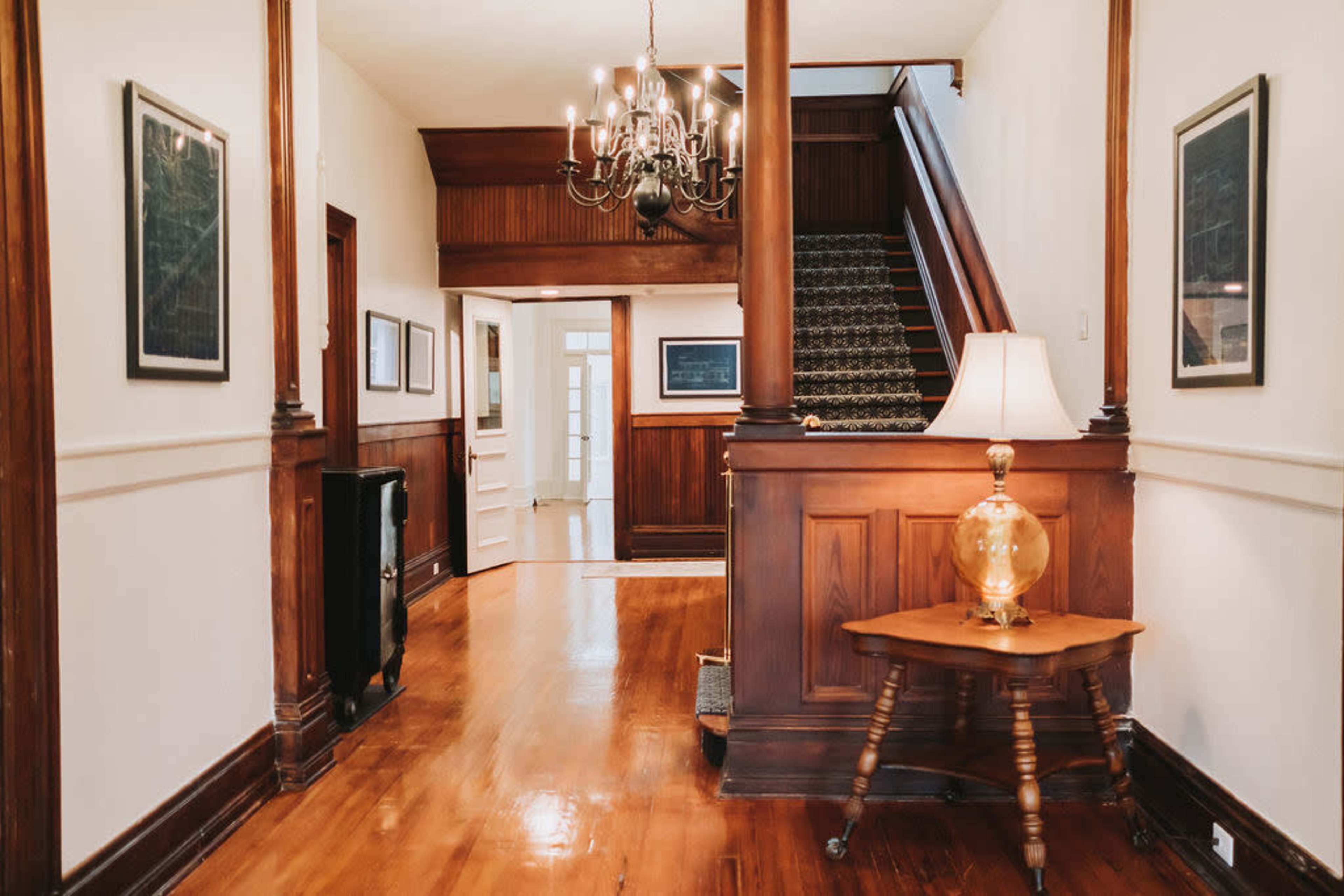 A hallway with wooden paneling, a chandelier, and a staircase leading to an upper floor.