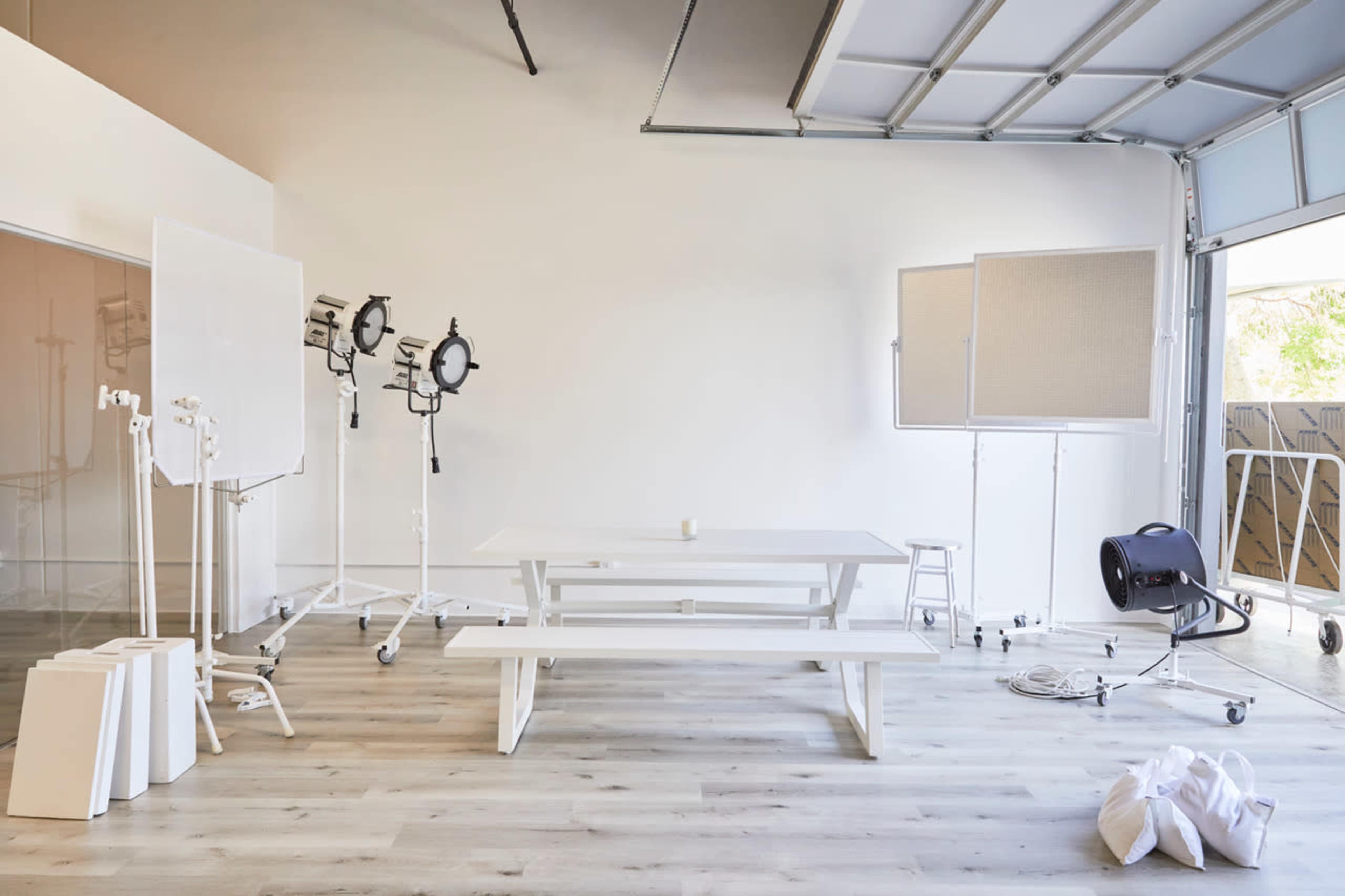 A bright, spacious studio with a wooden table surrounded by various photography equipment, including lights and reflectors.