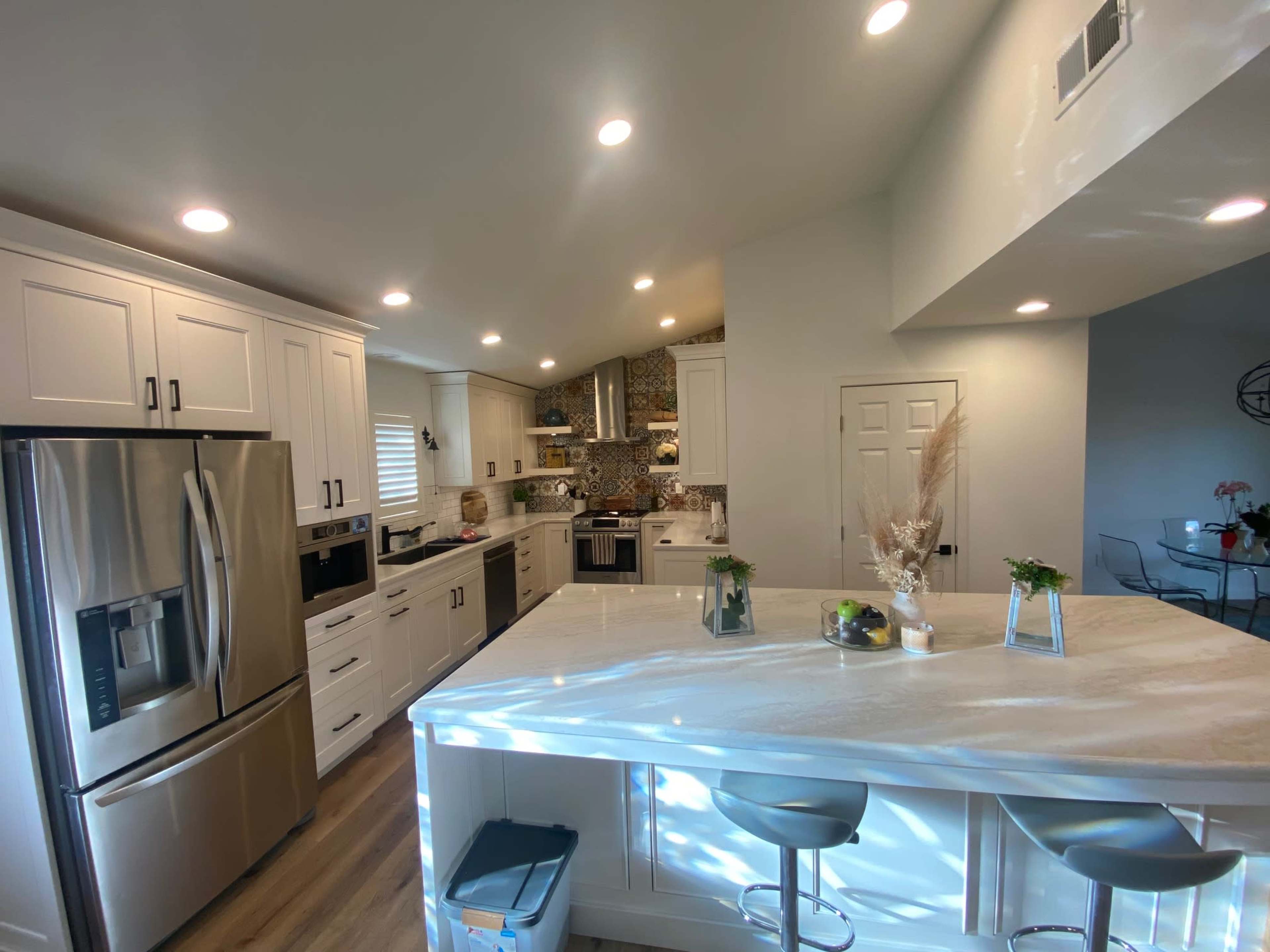 A modern kitchen features white cabinets, stainless steel appliances, and a large island with bar seating.