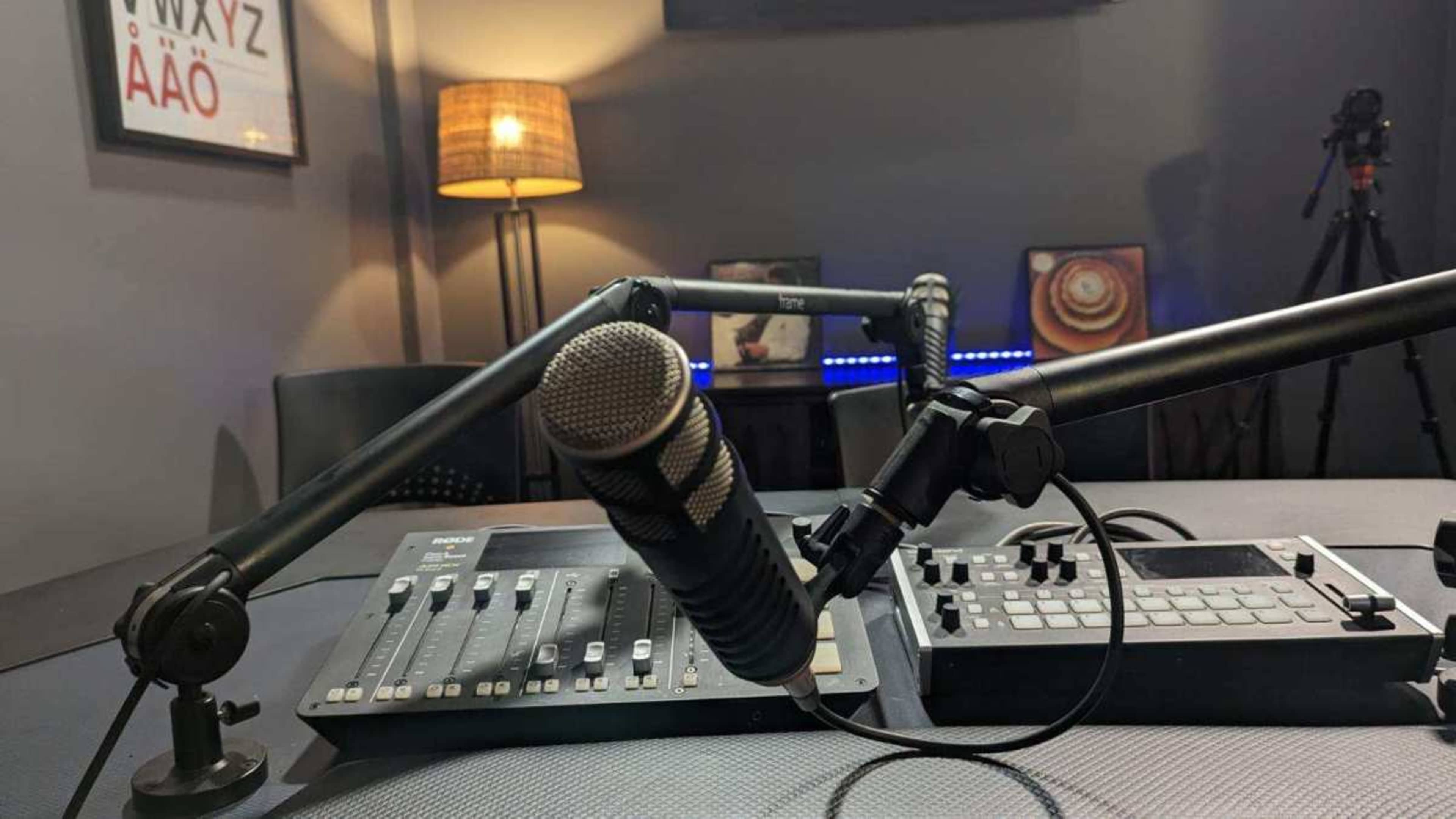 A microphone is positioned on an adjustable arm next to a sound mixer in a dimly lit studio.