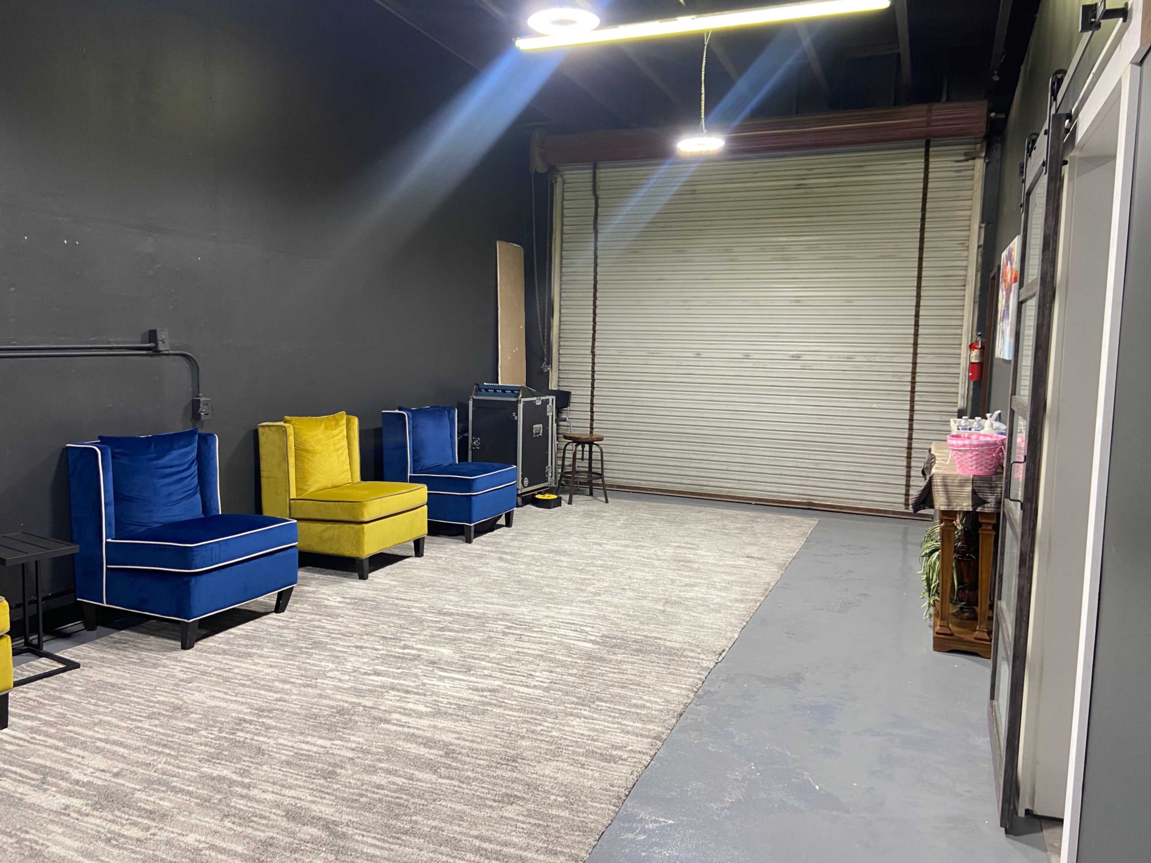 An interior space with two blue chairs and one yellow chair arranged along a gray rug, facing a closed metal garage door.