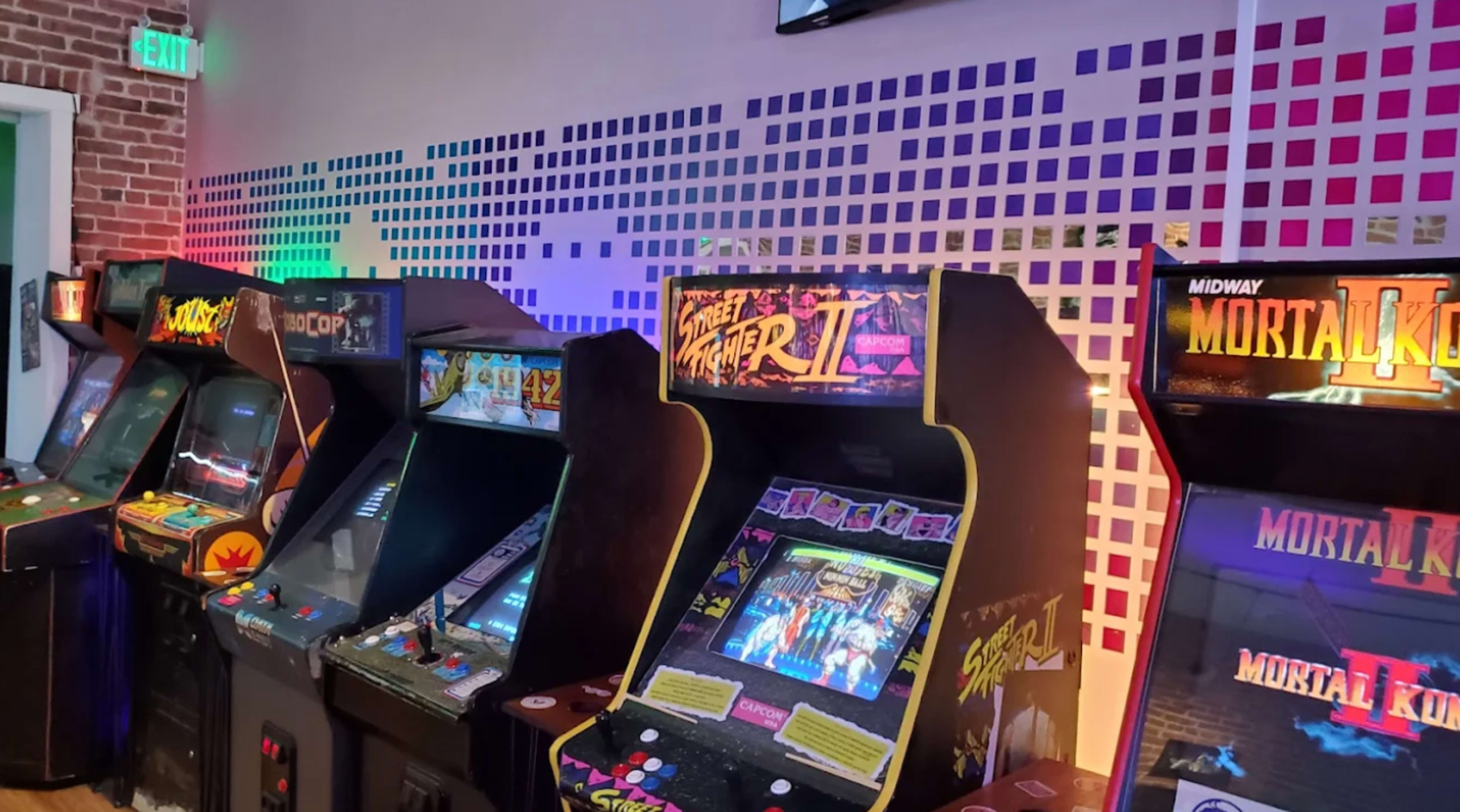 The image shows a row of classic arcade game cabinets, including "Street Fighter II" and "Mortal Kombat," set against a colorful wall with geometric designs.