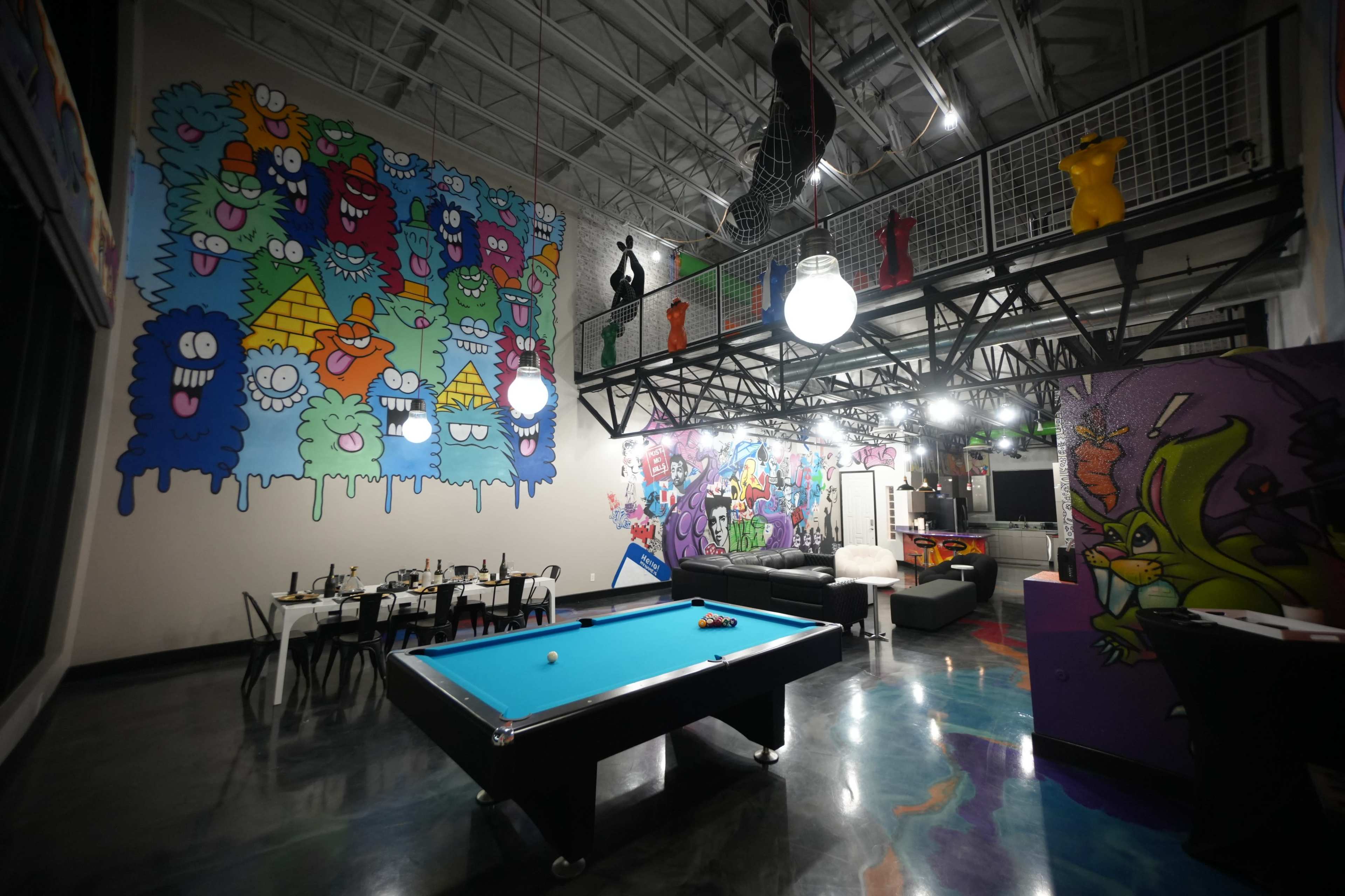 The image shows a vibrant, modern game room with colorful murals on the walls, a billiards table in the center, and tables set for dining.