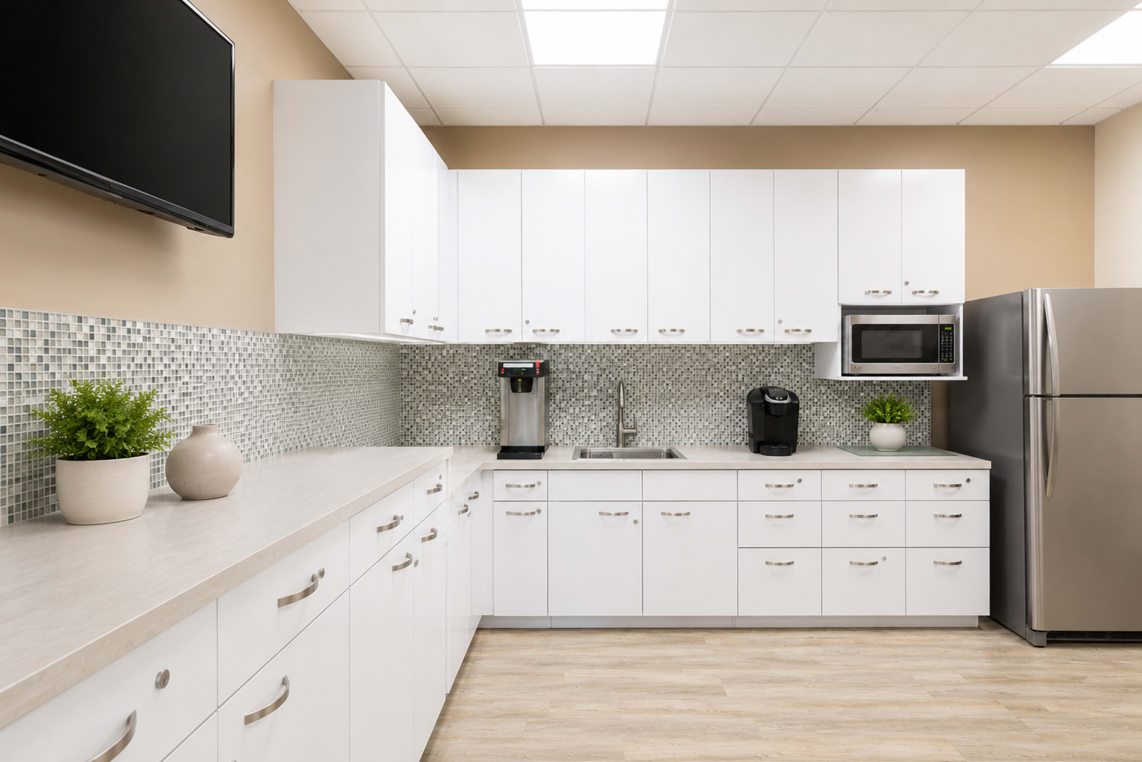The image shows a modern kitchen with white cabinetry, a stainless steel refrigerator, a coffee maker, and a tiled backsplash.