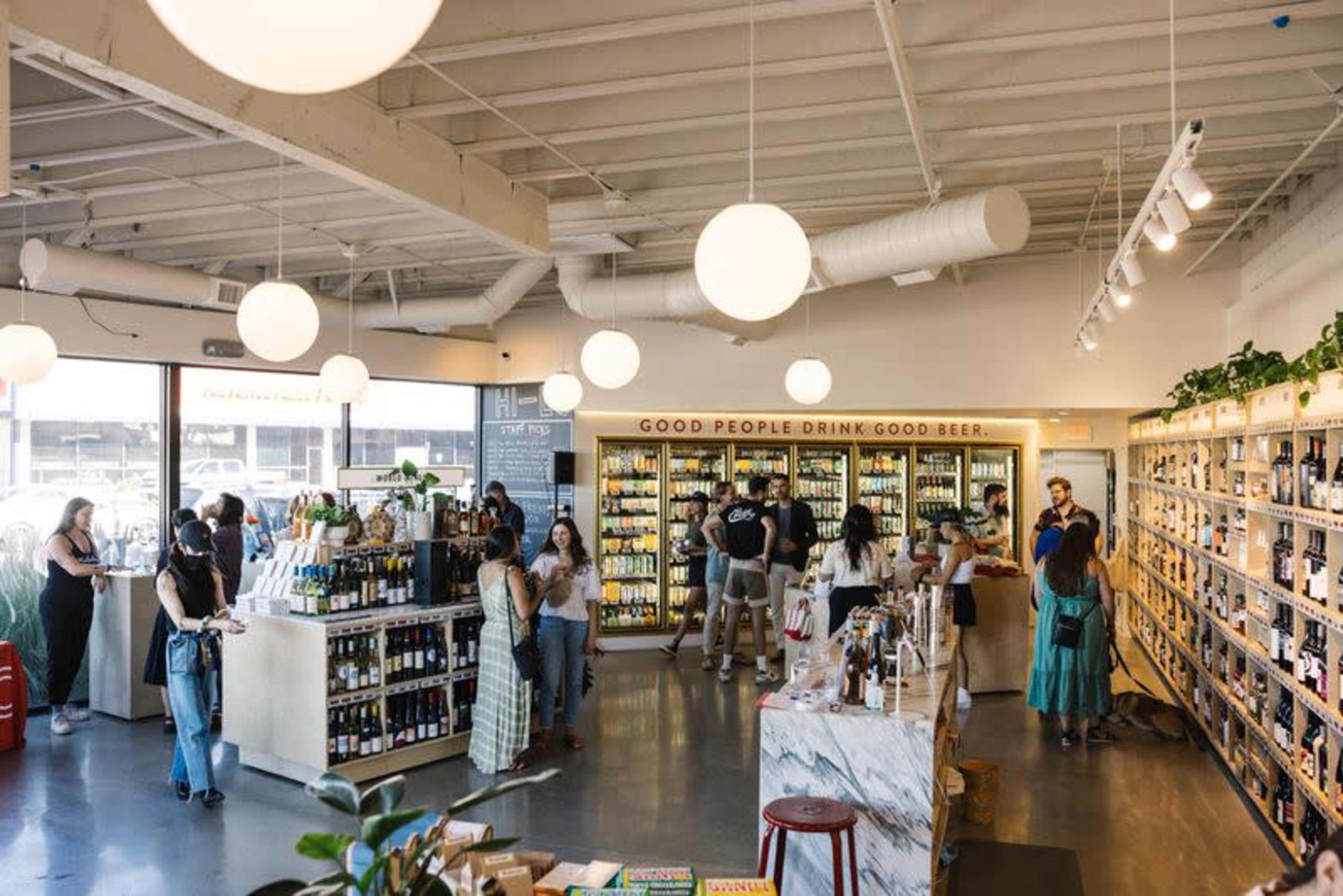 The image features a busy craft beverage shop with shelves filled with various drinks, illuminated by round pendant lights.