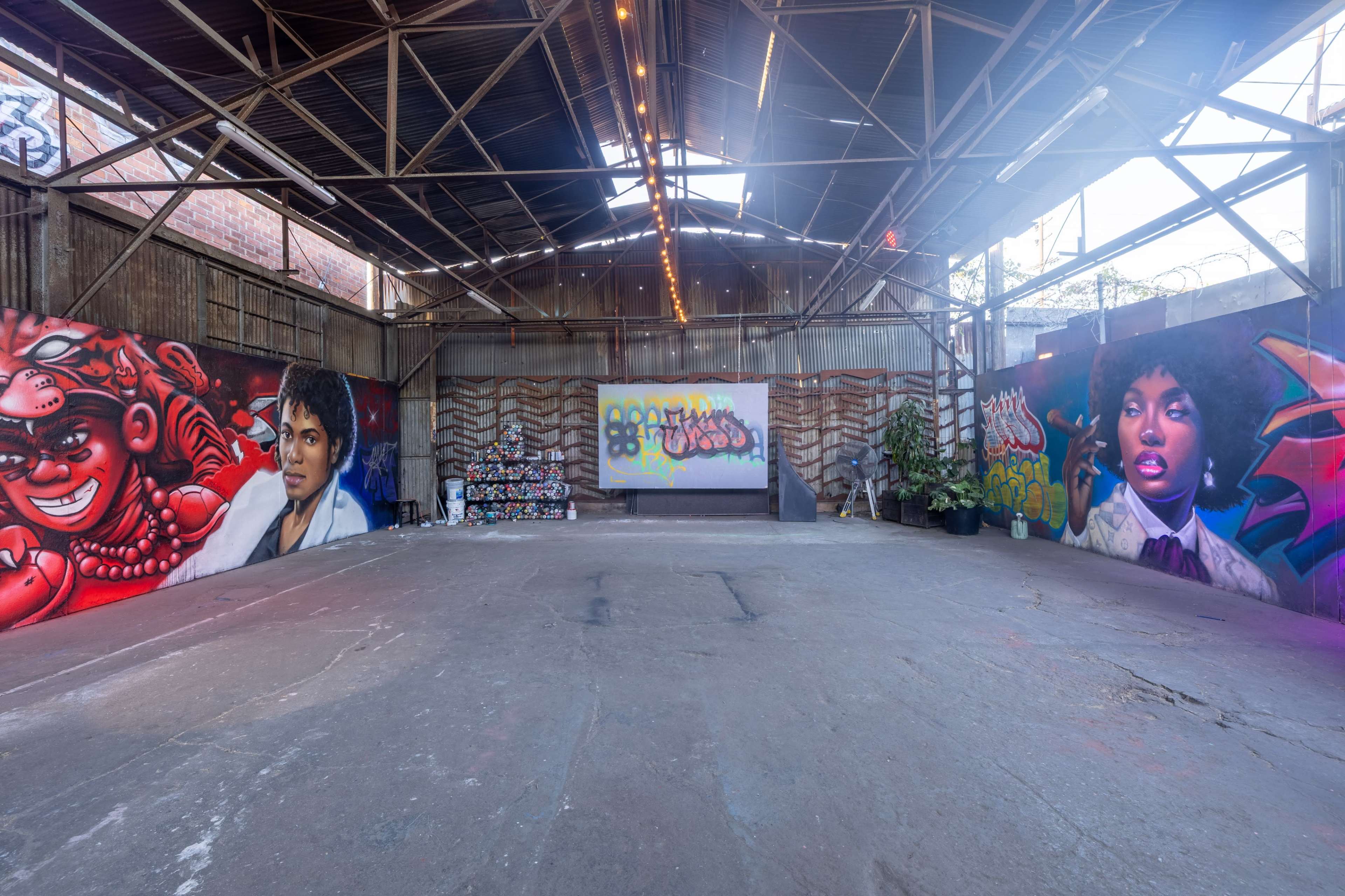 The image shows a spacious, industrial-style interior with colorful graffiti murals on the walls and a clear area in the center.