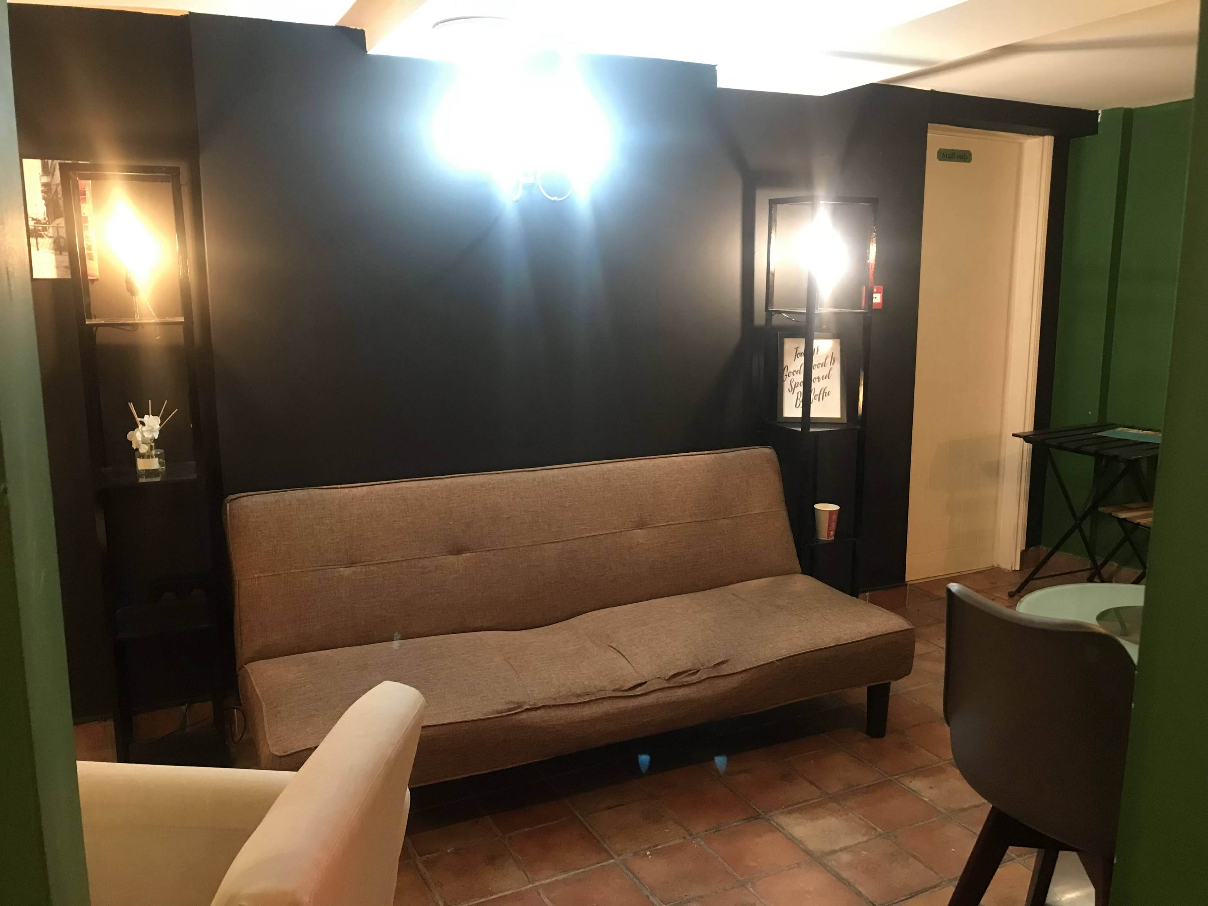 A small, cozy room featuring a brown sofa, two display shelves with lights, and a small table in the corner.