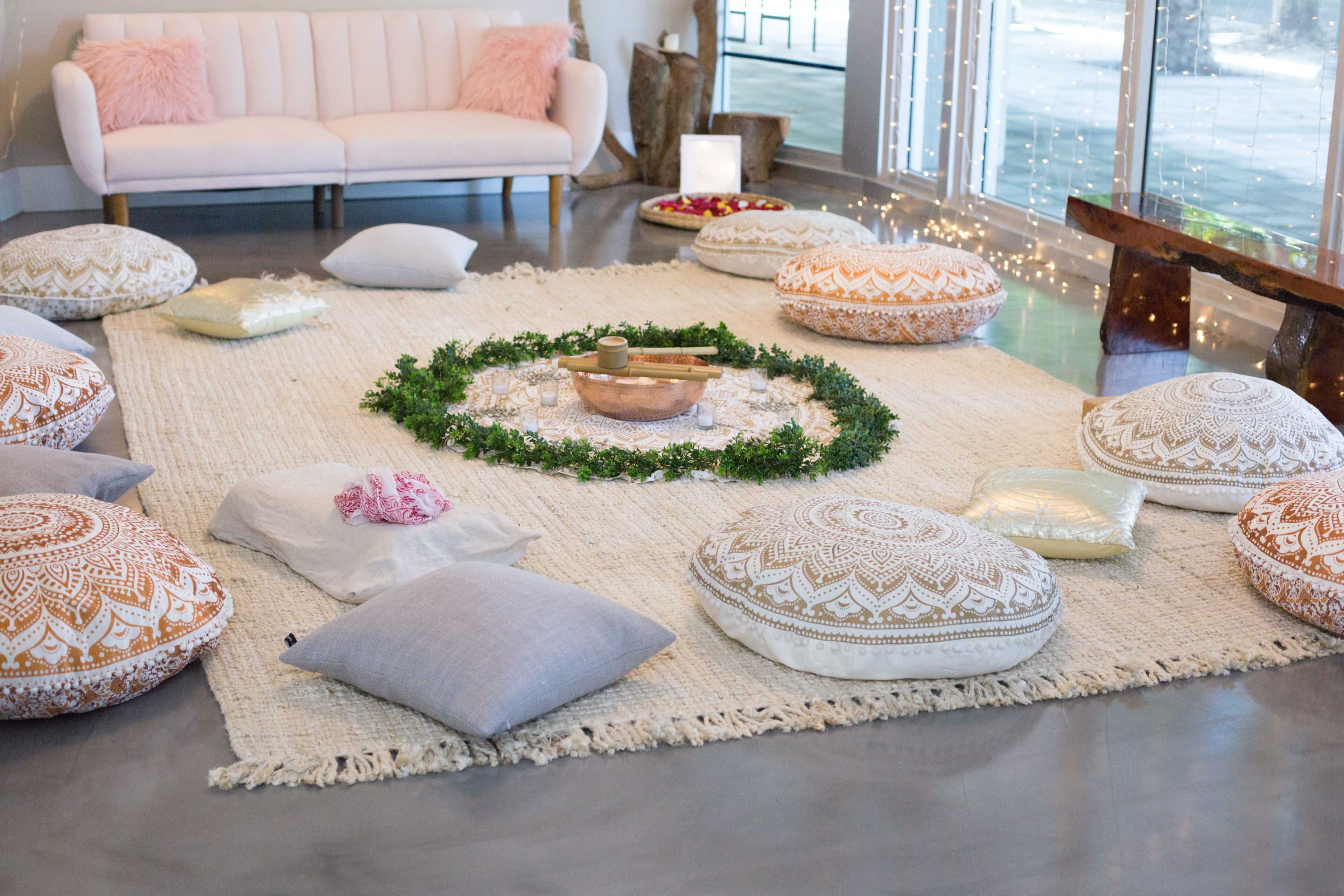 A cozy meditation space features circular, patterned cushions arranged around a central area with greenery and a decorative bowl on a textured rug.