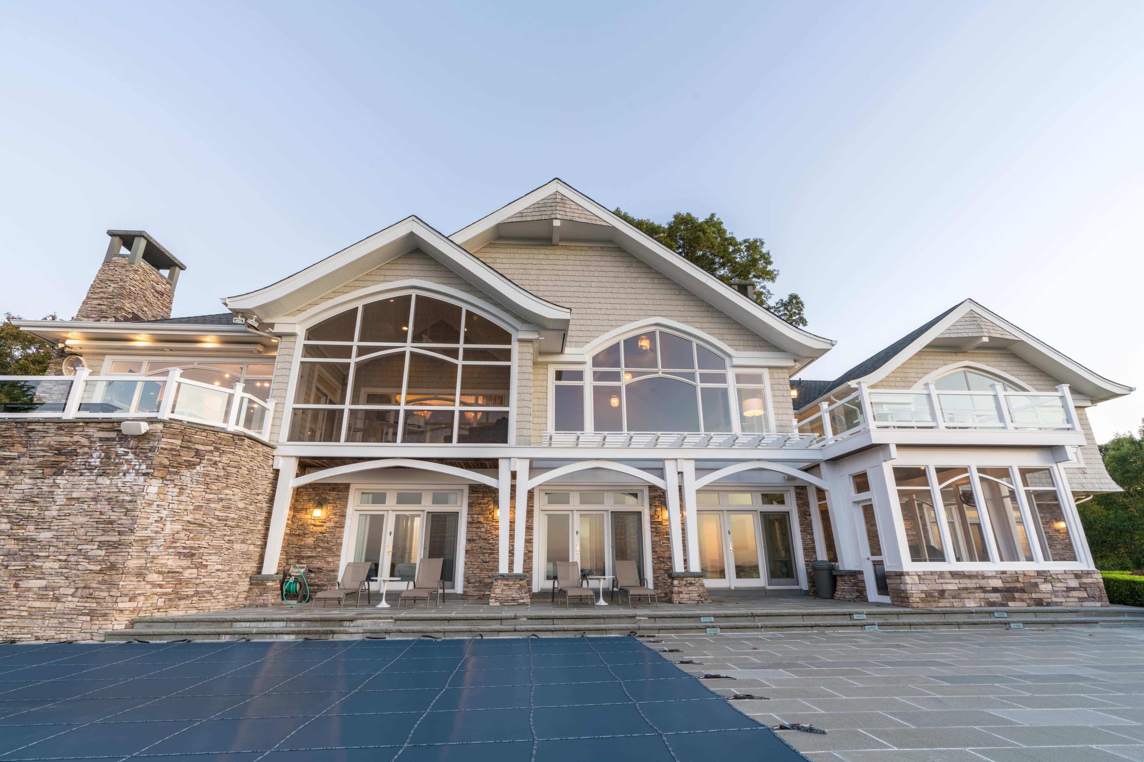 The image shows a large, modern house with a stone facade and multiple large windows, set against a clear sky.