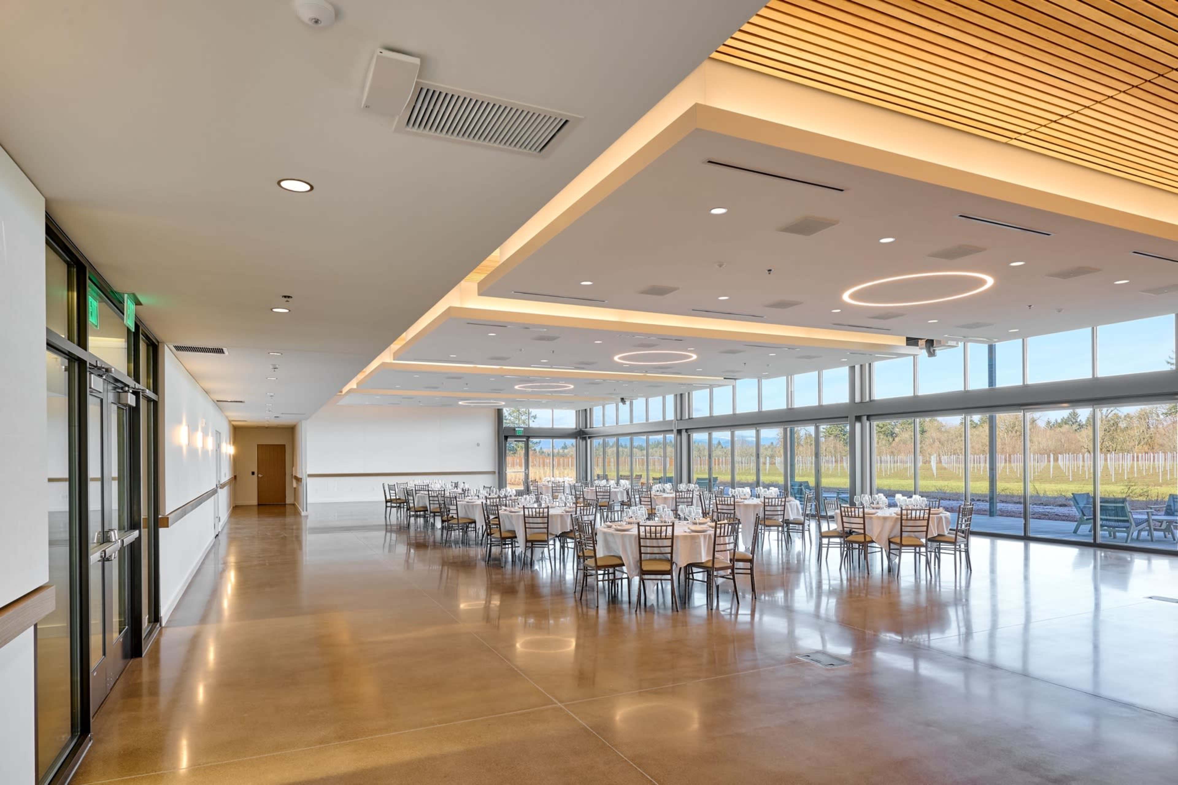 The image shows a spacious banquet hall with large windows, modern lighting, and rows of tables set up for an event.