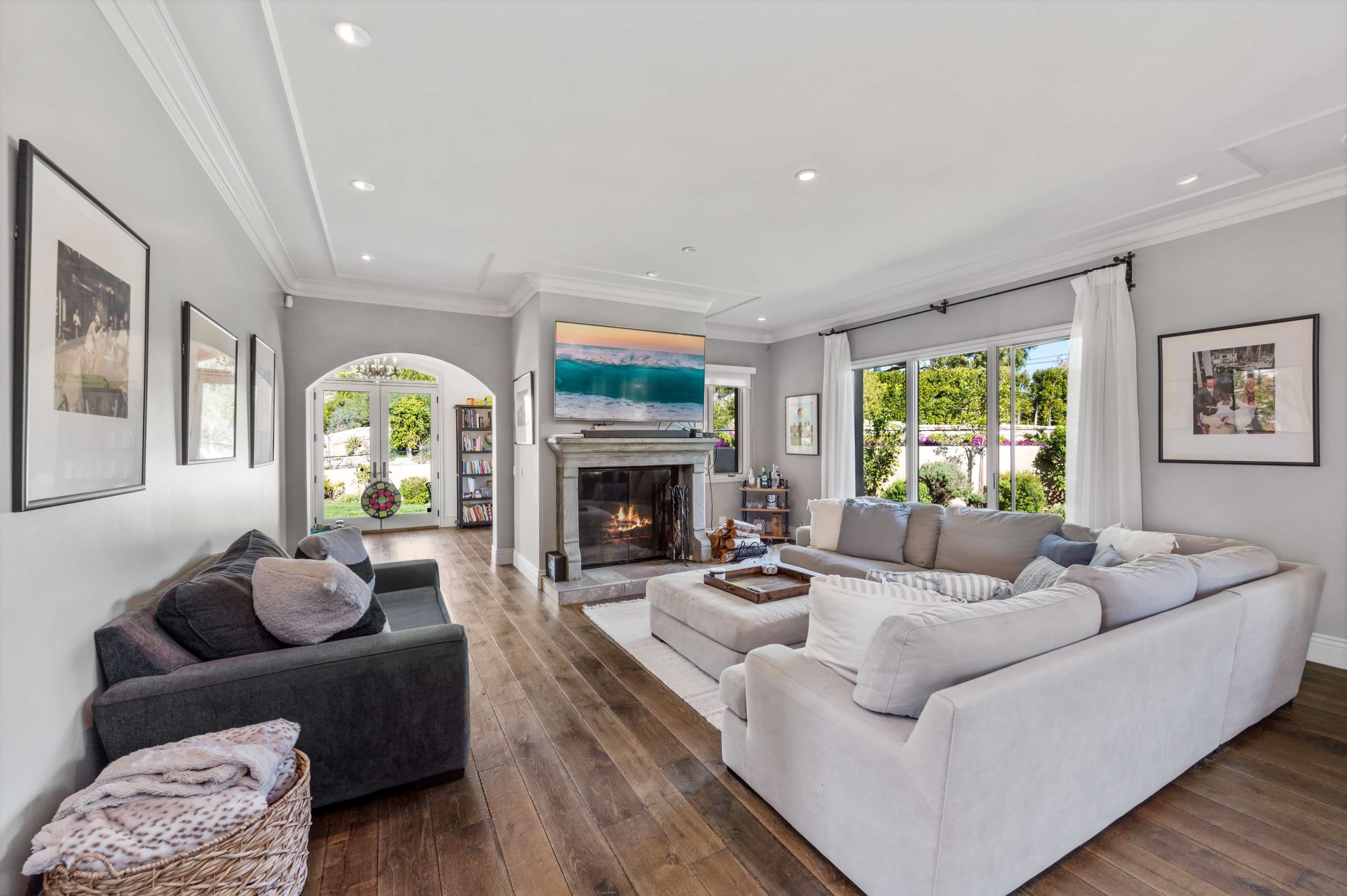 A modern living room with a large sectional sofa, a fireplace, and a view of the outdoor garden through glass doors.