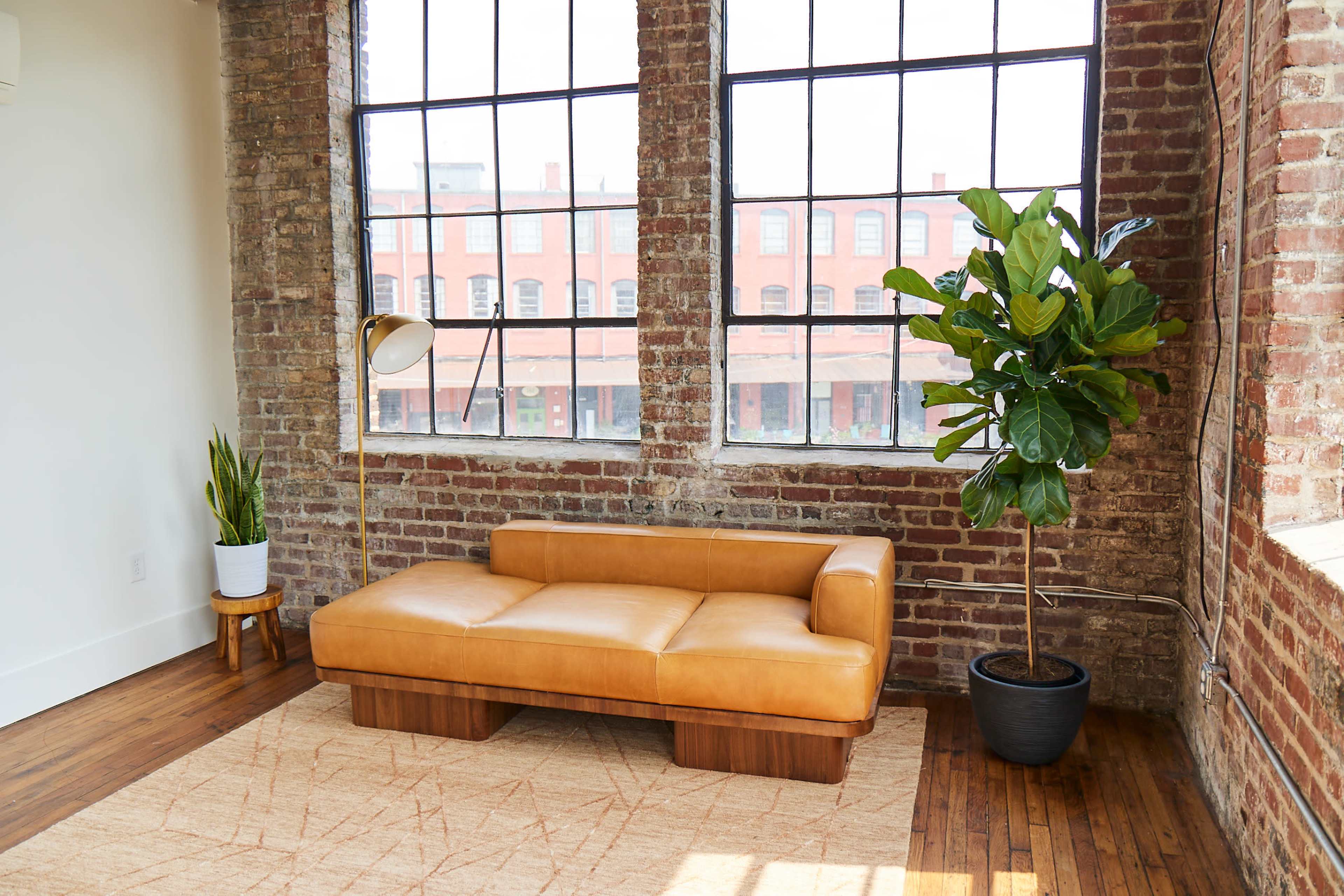 A modern living space with a leather sofa, a floor lamp, and large windows that overlook a brick building exterior.
