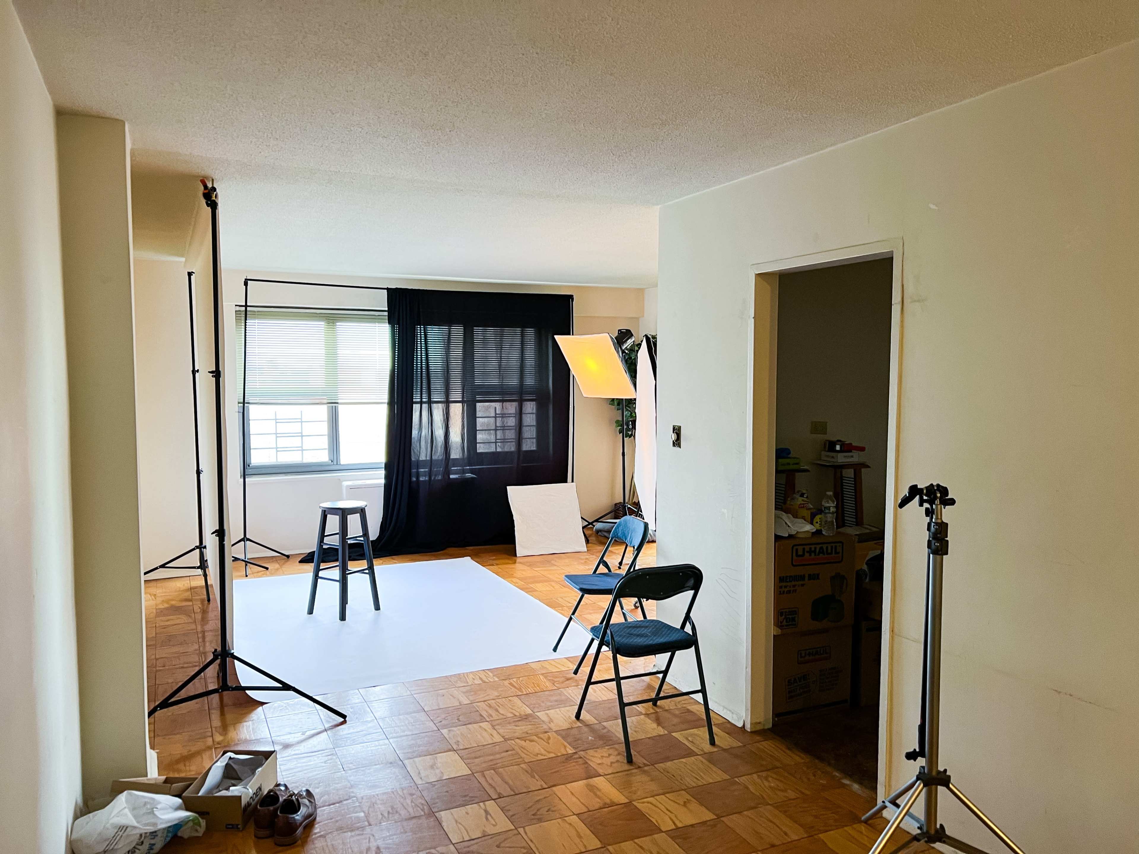 A photo studio setup in a room with a black curtain, a stool, two chairs, and lighting equipment.