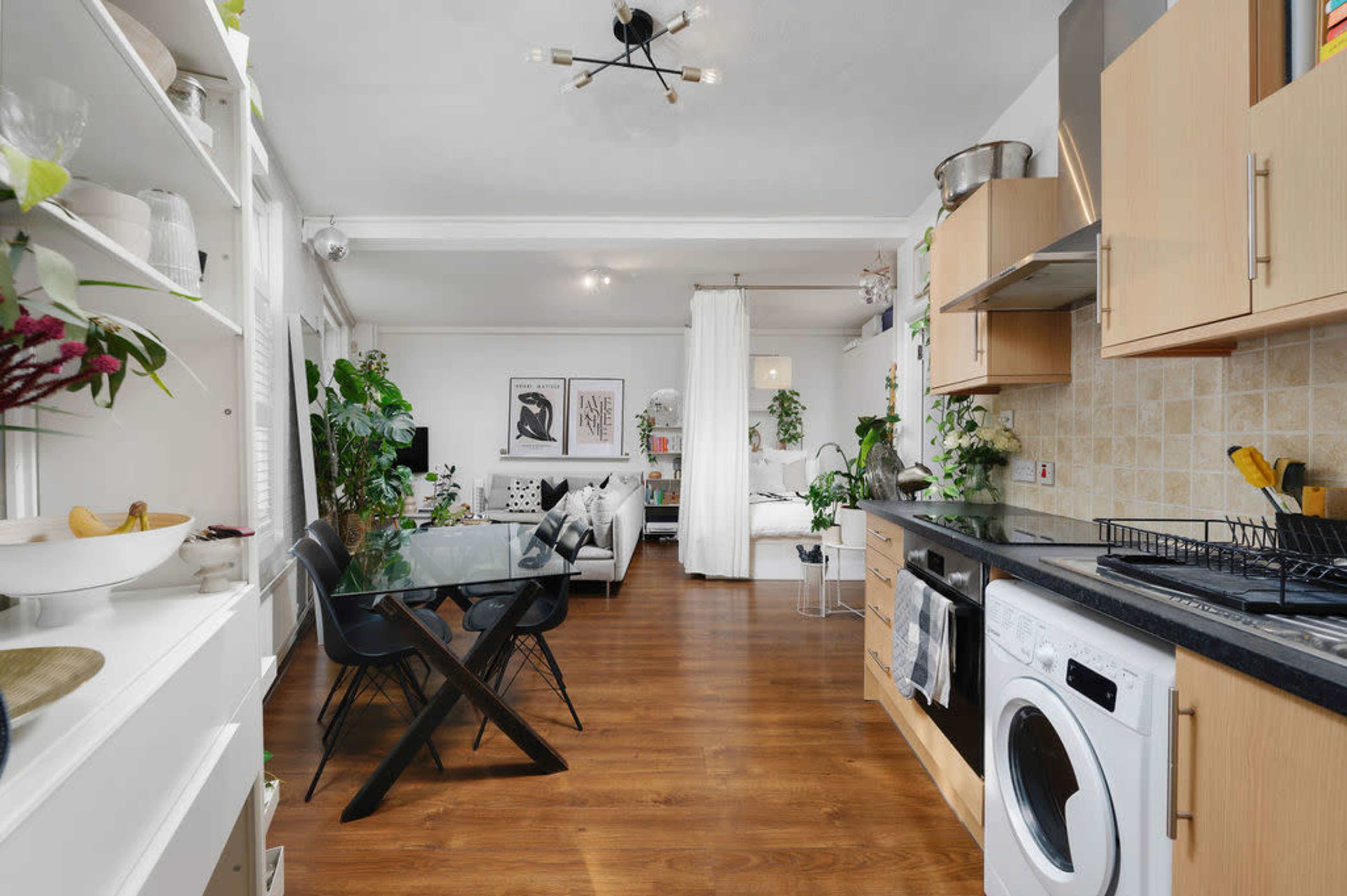 A modern open-concept kitchen and living area features wooden floors, sleek cabinetry, and large windows allowing natural light to fill the space.