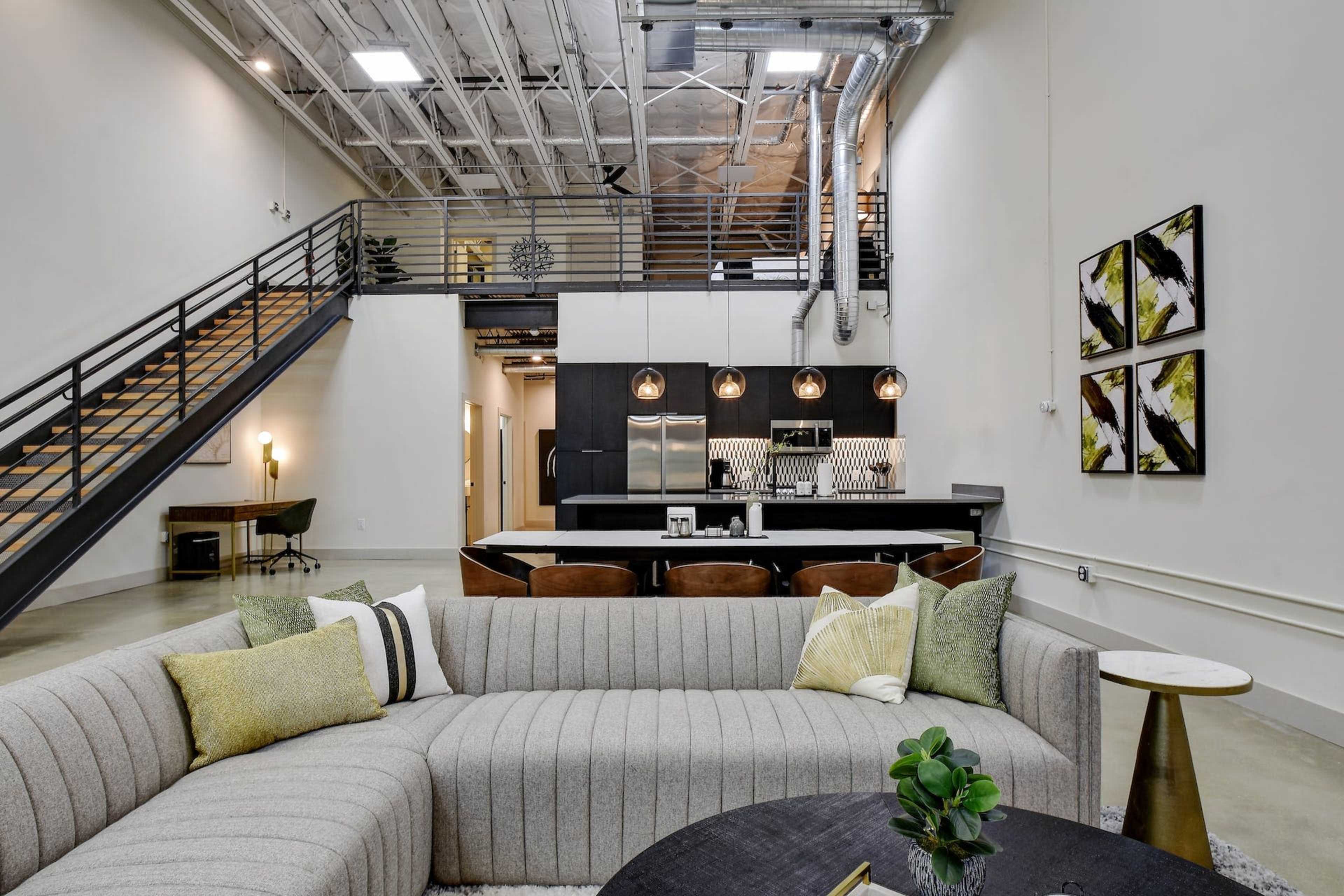 A contemporary open-concept living area with a large sectional sofa, a kitchen in the background, and a staircase leading to an upper level.