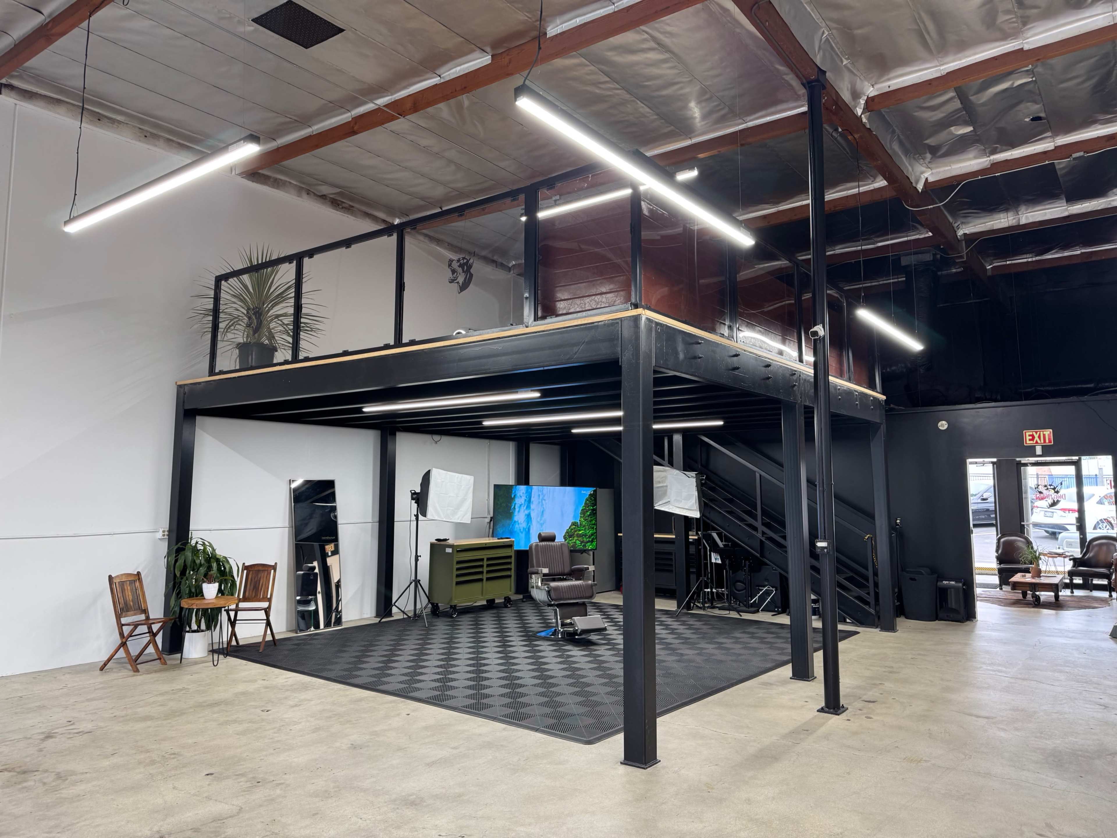 The image shows a spacious office interior with a raised platform featuring a seating area, large windows, and various lighting equipment on the ground floor.