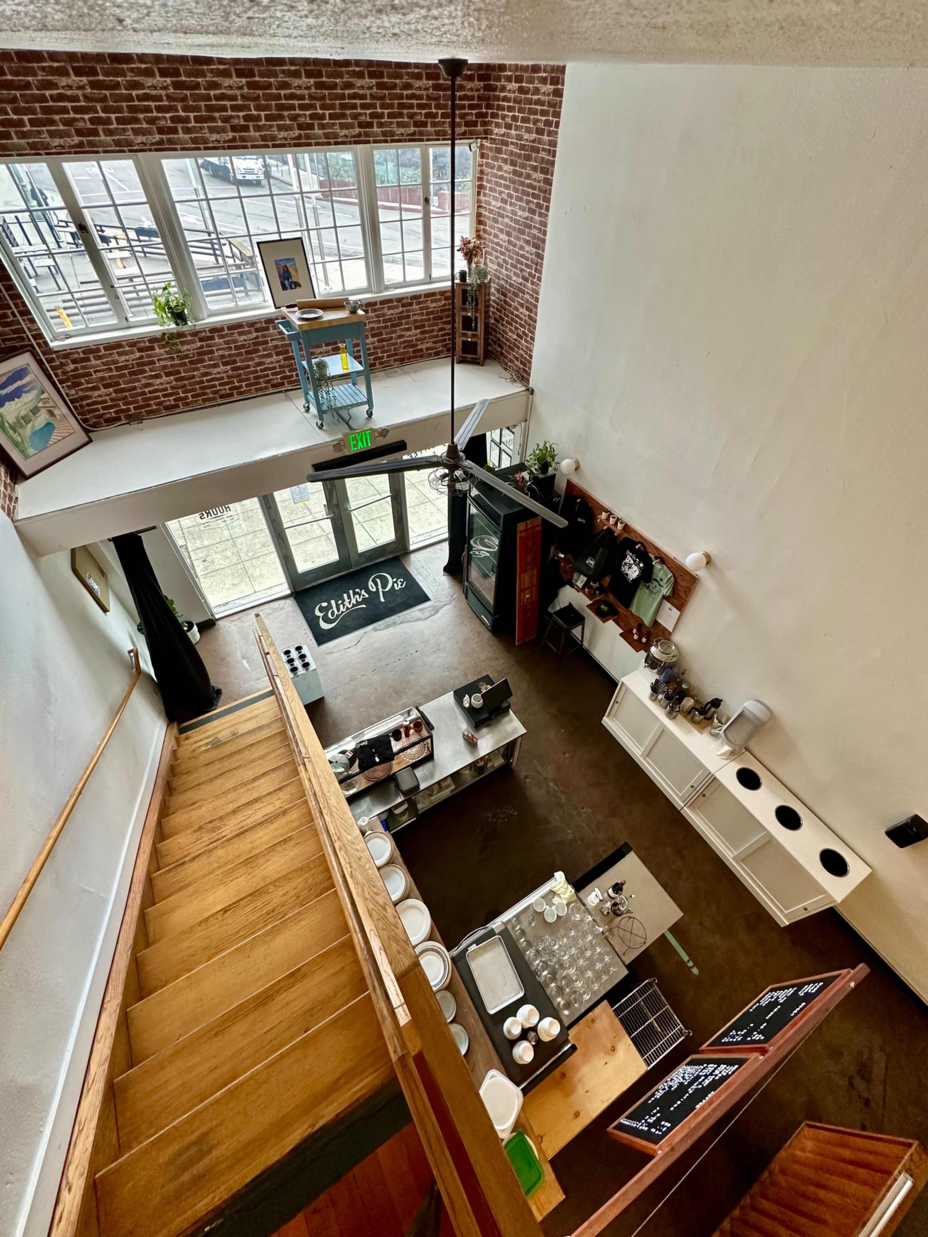An interior view of a cafe with a staircase, a service counter, and large windows allowing natural light to enter.