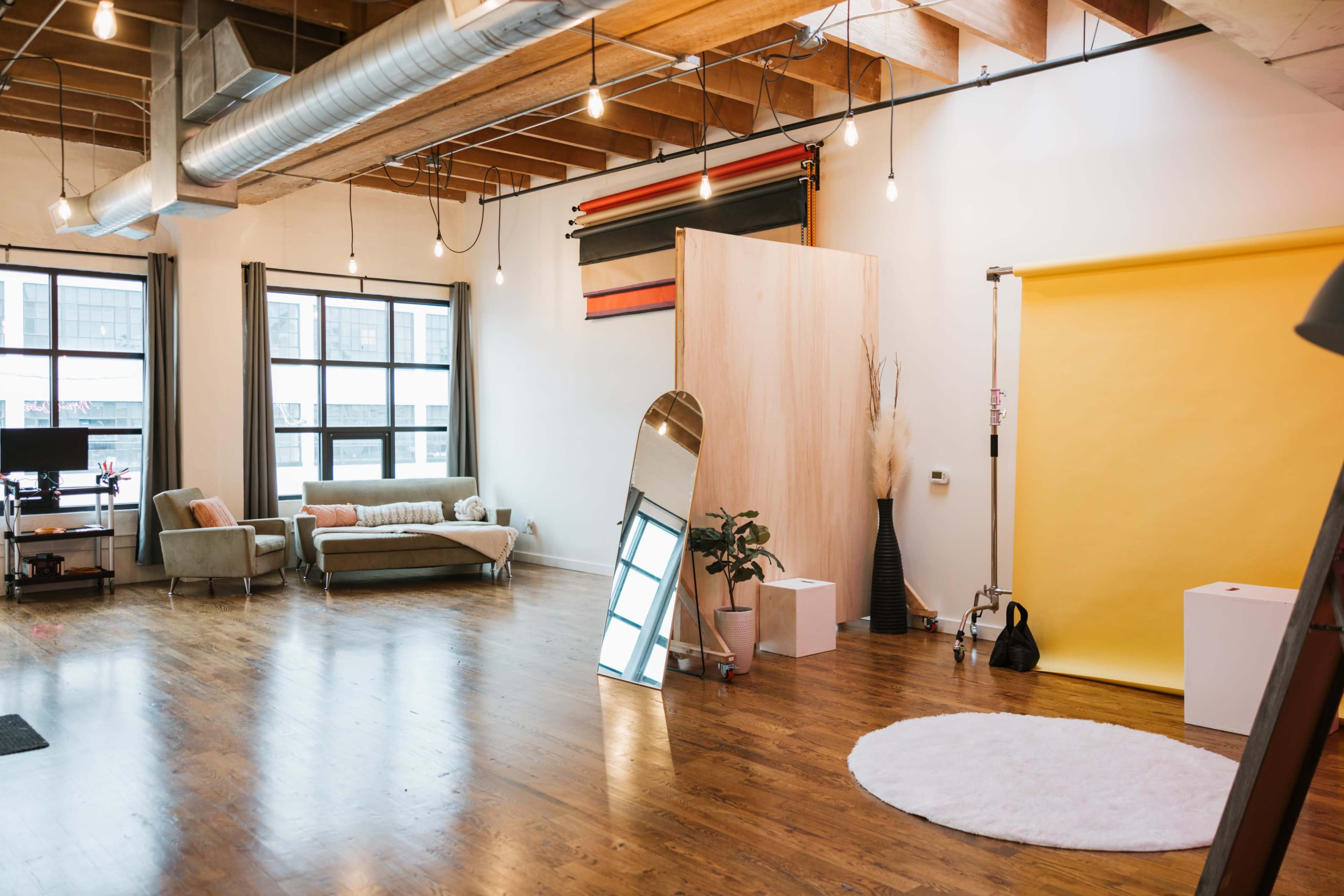A spacious, well-lit studio with wooden floors, large windows, and a yellow backdrop for photography.