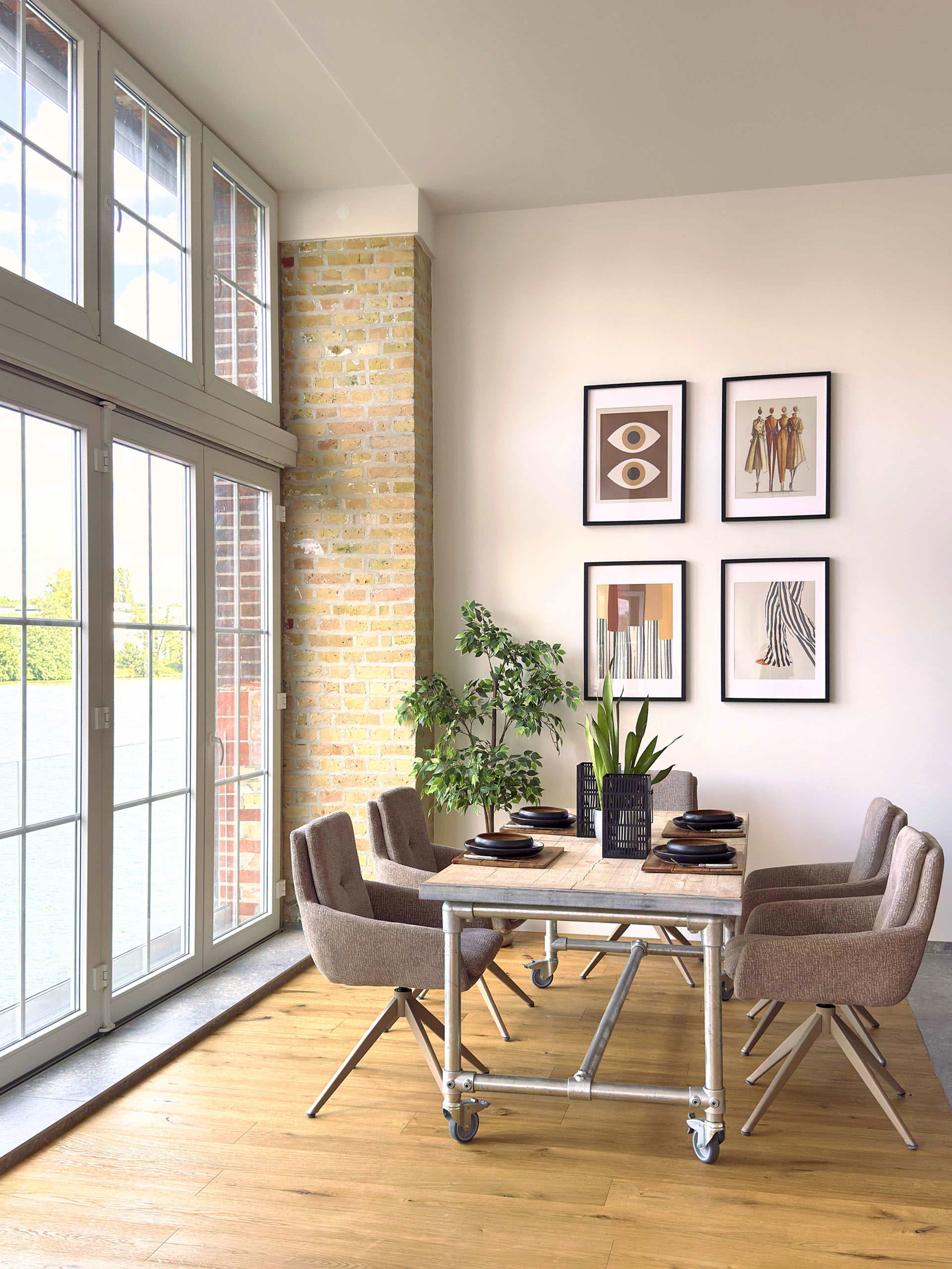 A modern dining area features a table surrounded by four brown upholstered chairs, with framed artwork on the wall and a potted plant nearby.