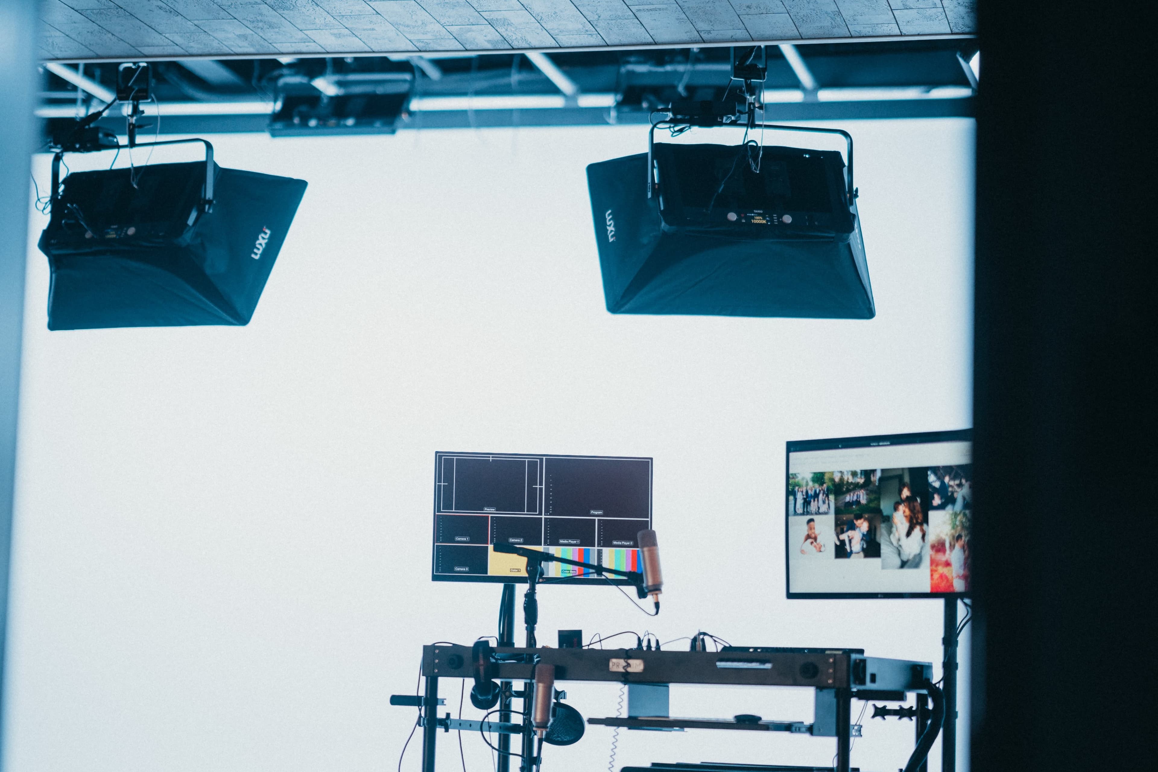 A production setup featuring two studio lights and two monitors displaying video feeds.