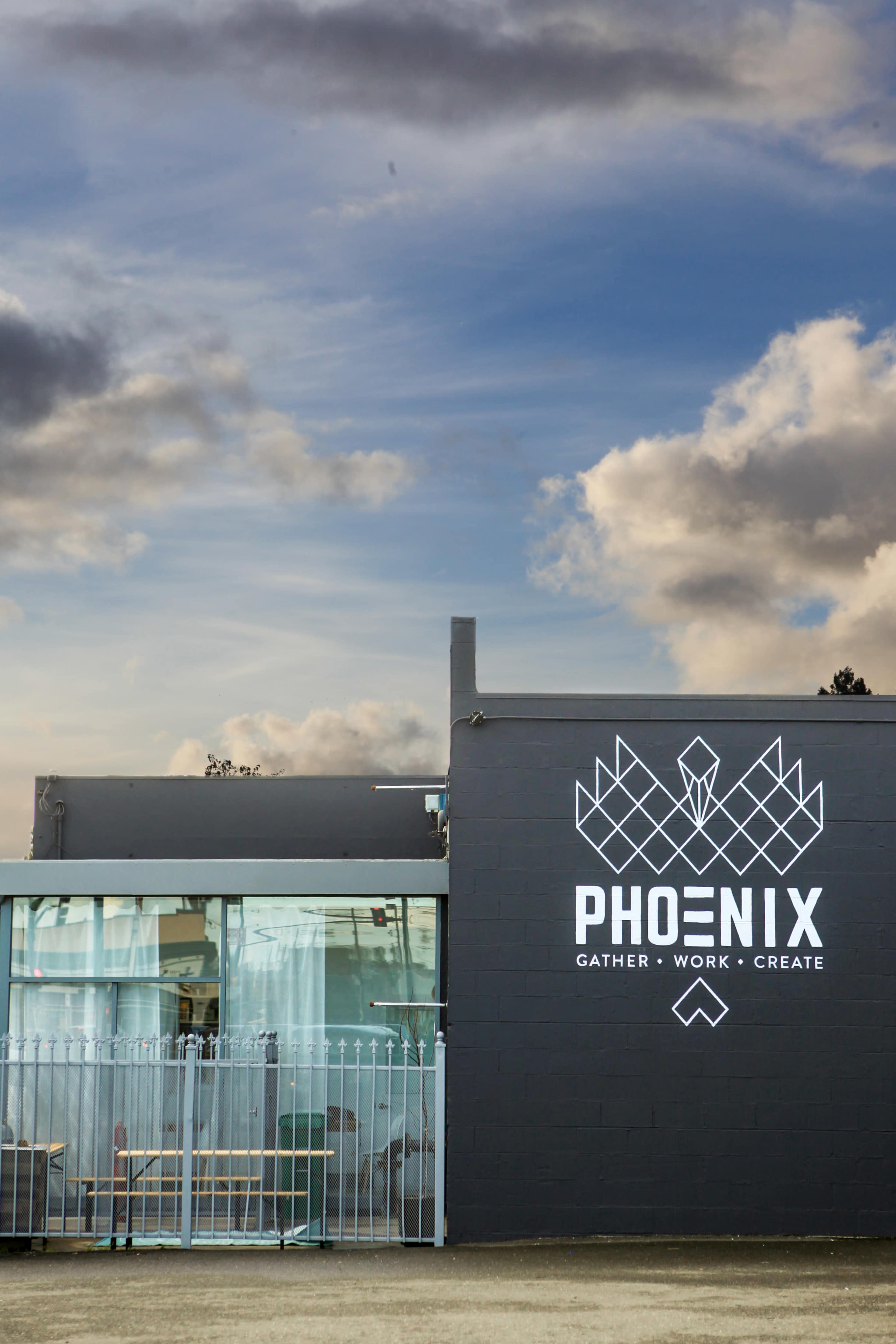 The image shows a modern building with the word "PHOENIX" prominently displayed on the wall, along with the tagline "GATHER • WORK • CREATE."