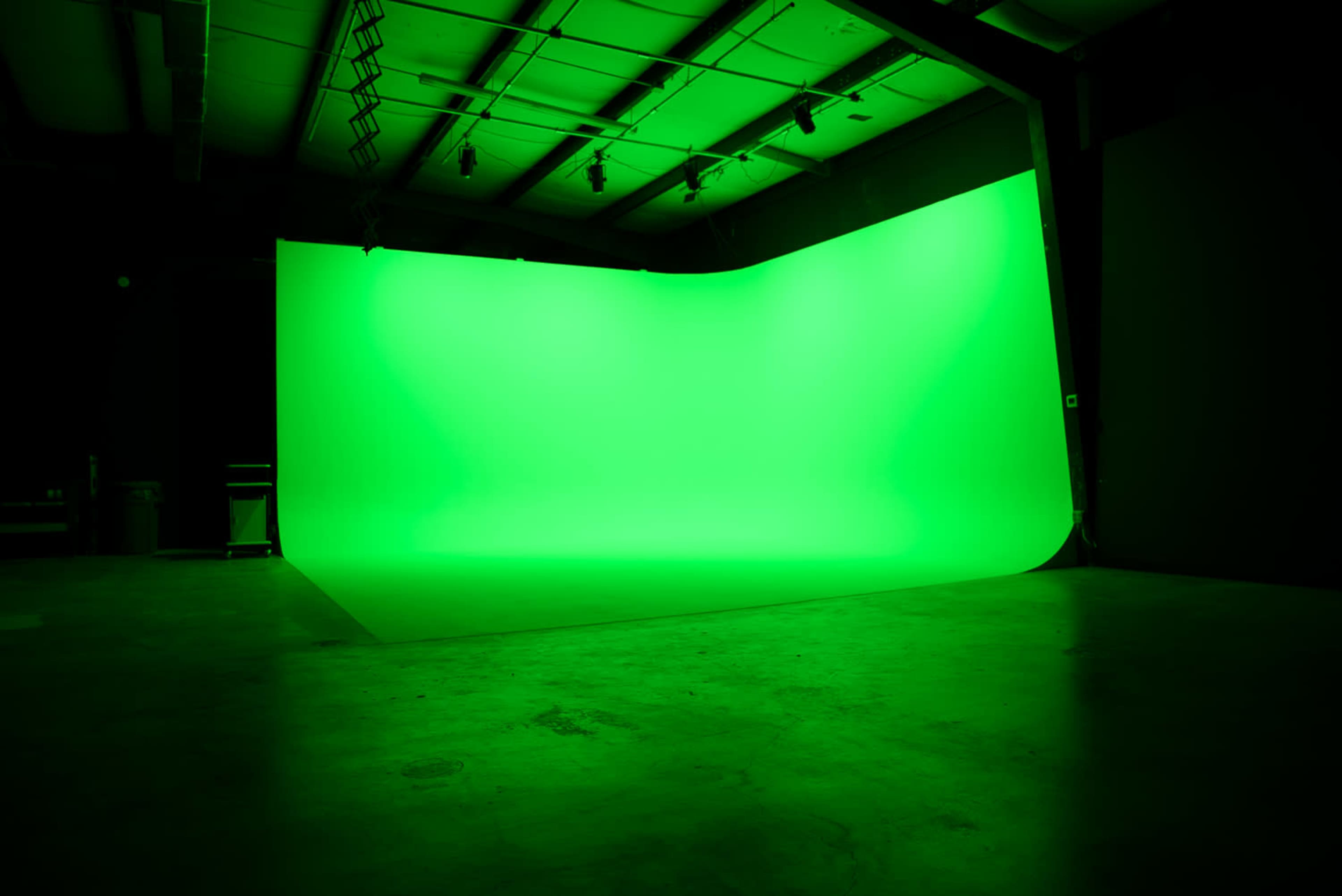 The image shows an empty studio space with a large green backdrop and polished concrete flooring.