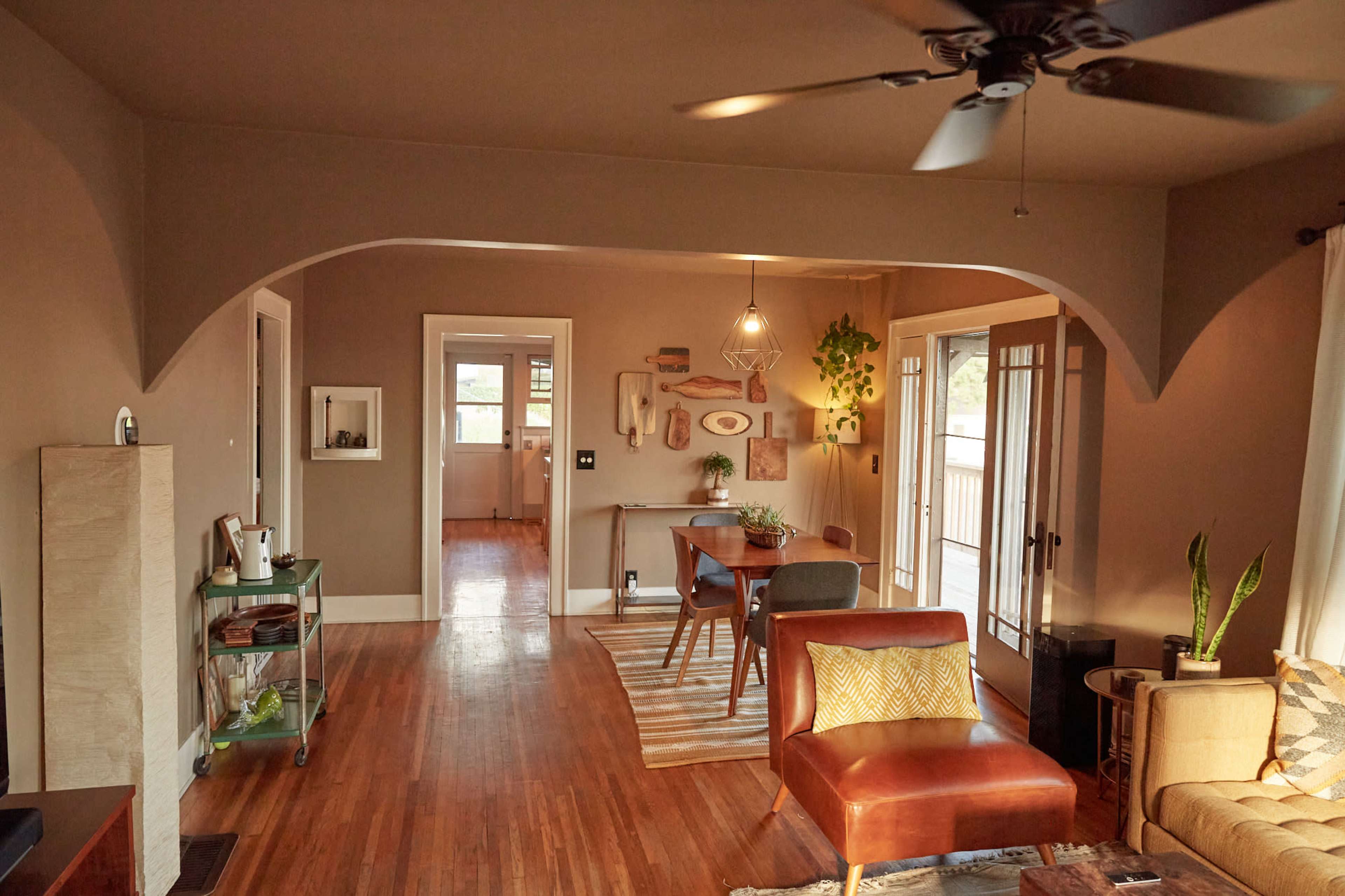 A modern living room with hardwood floors, a dining area visible in the background, and a blend of furniture and decorative elements.