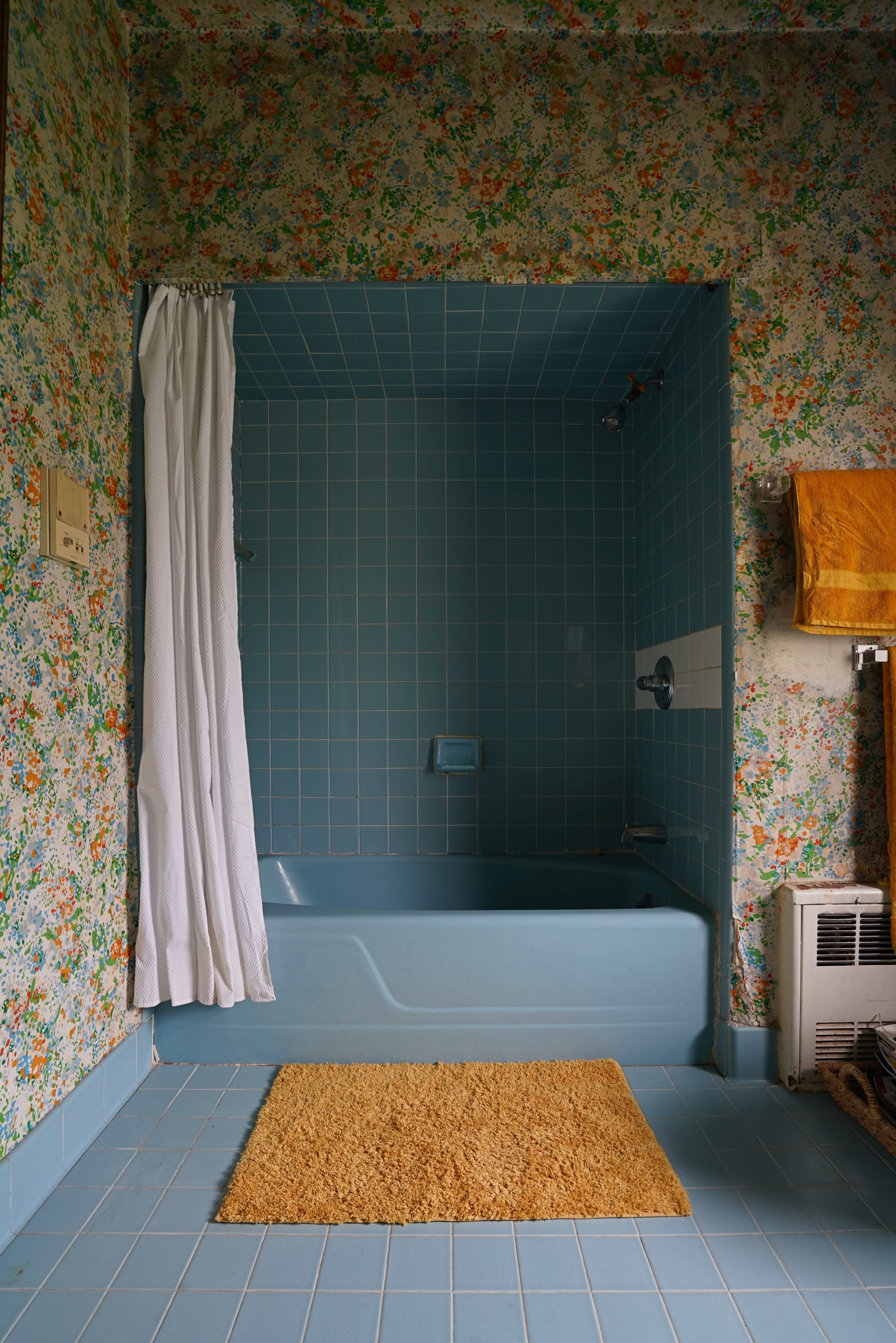 A bathroom featuring a blue bathtub, floral wallpaper, and a beige bath mat on a blue tiled floor.