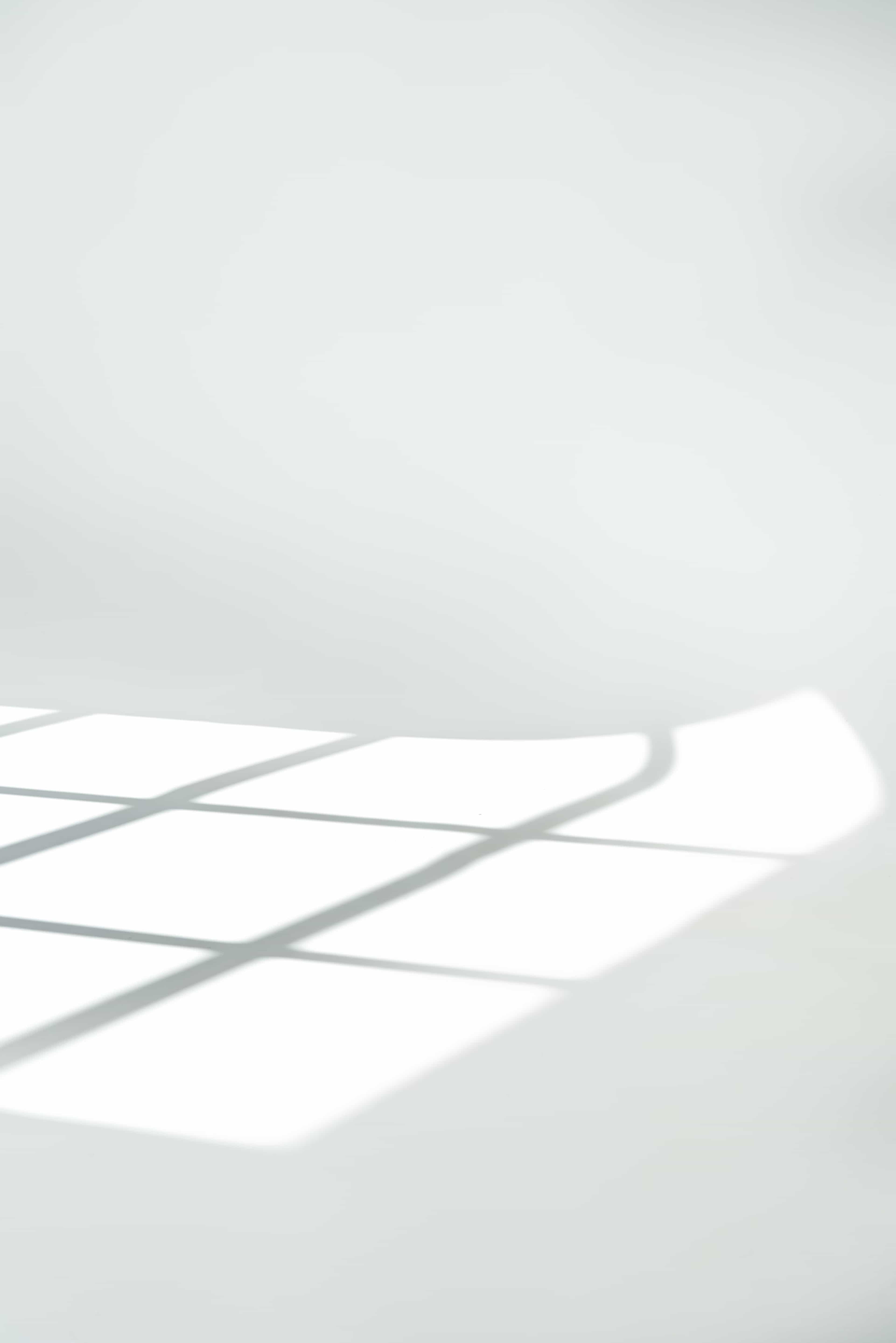 A geometric pattern of shadows forms on a white surface from sunlight streaming through a window.