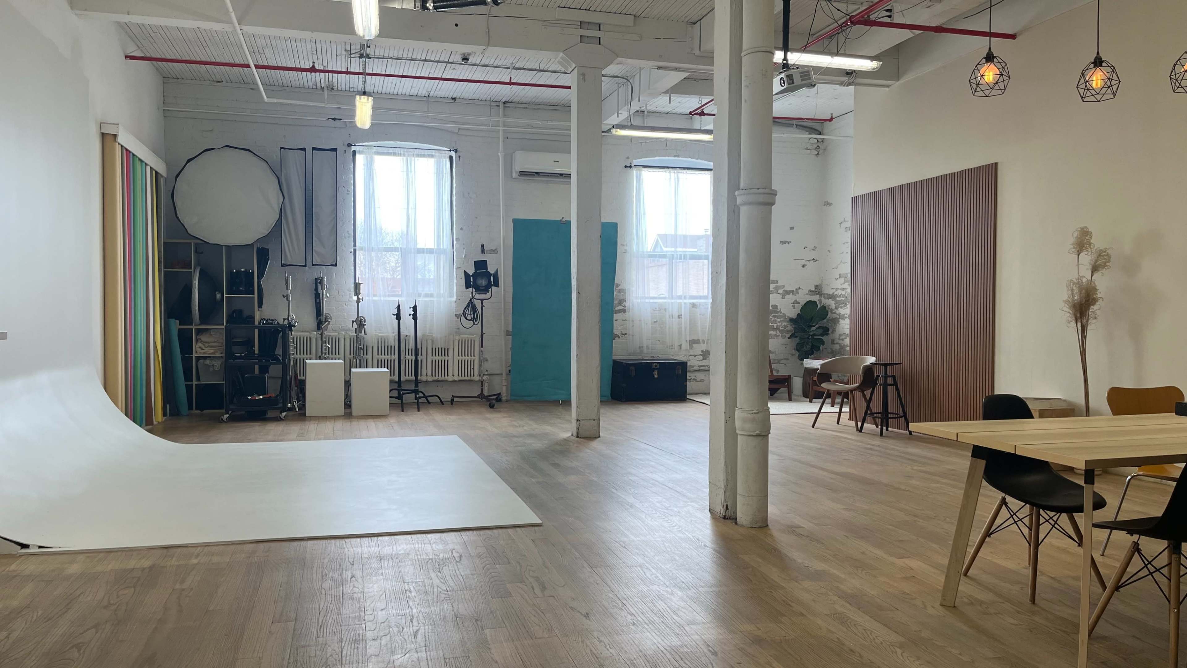 A spacious, well-lit studio with wooden floors, large windows, and various photography equipment arranged along the walls.
