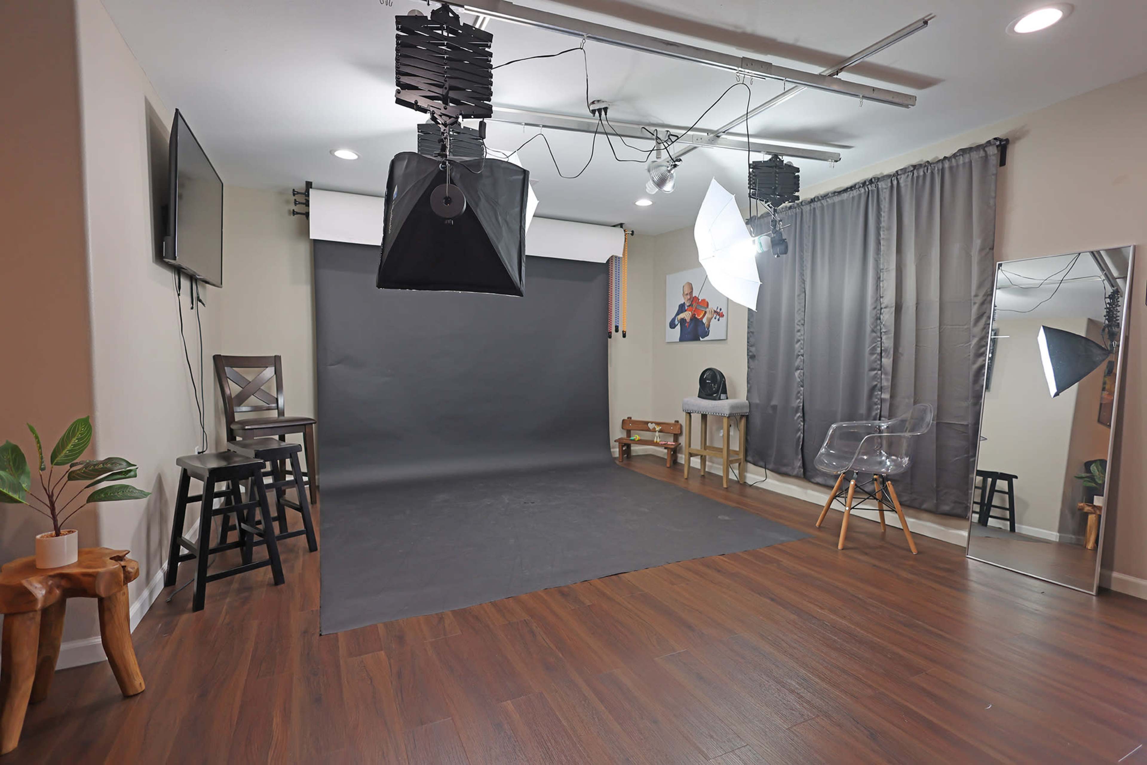 A photography studio with a gray backdrop, lighting equipment, a mirror, and wooden flooring.