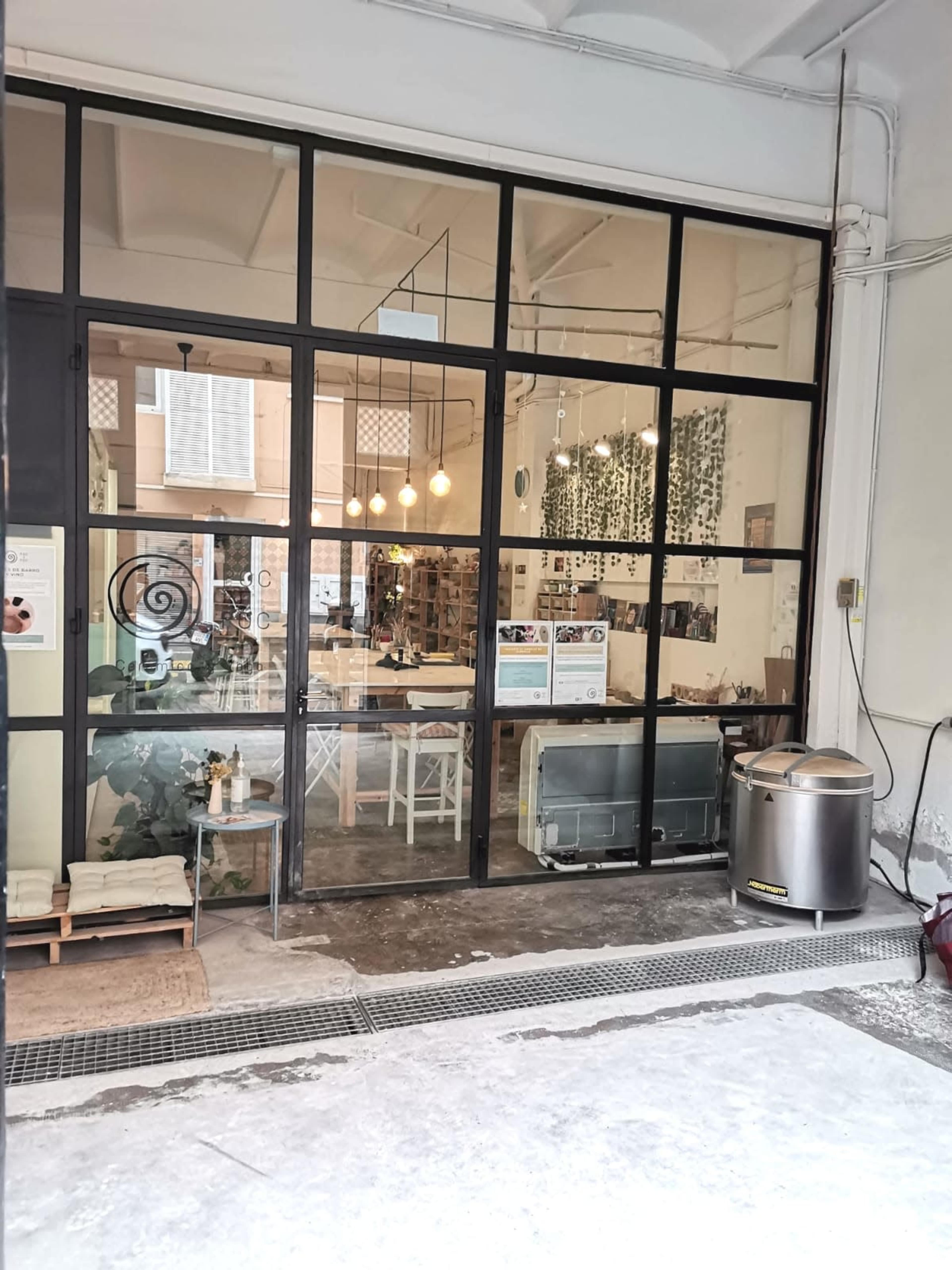 A modern café with large glass windows, revealing a cozy interior filled with plants and furniture.