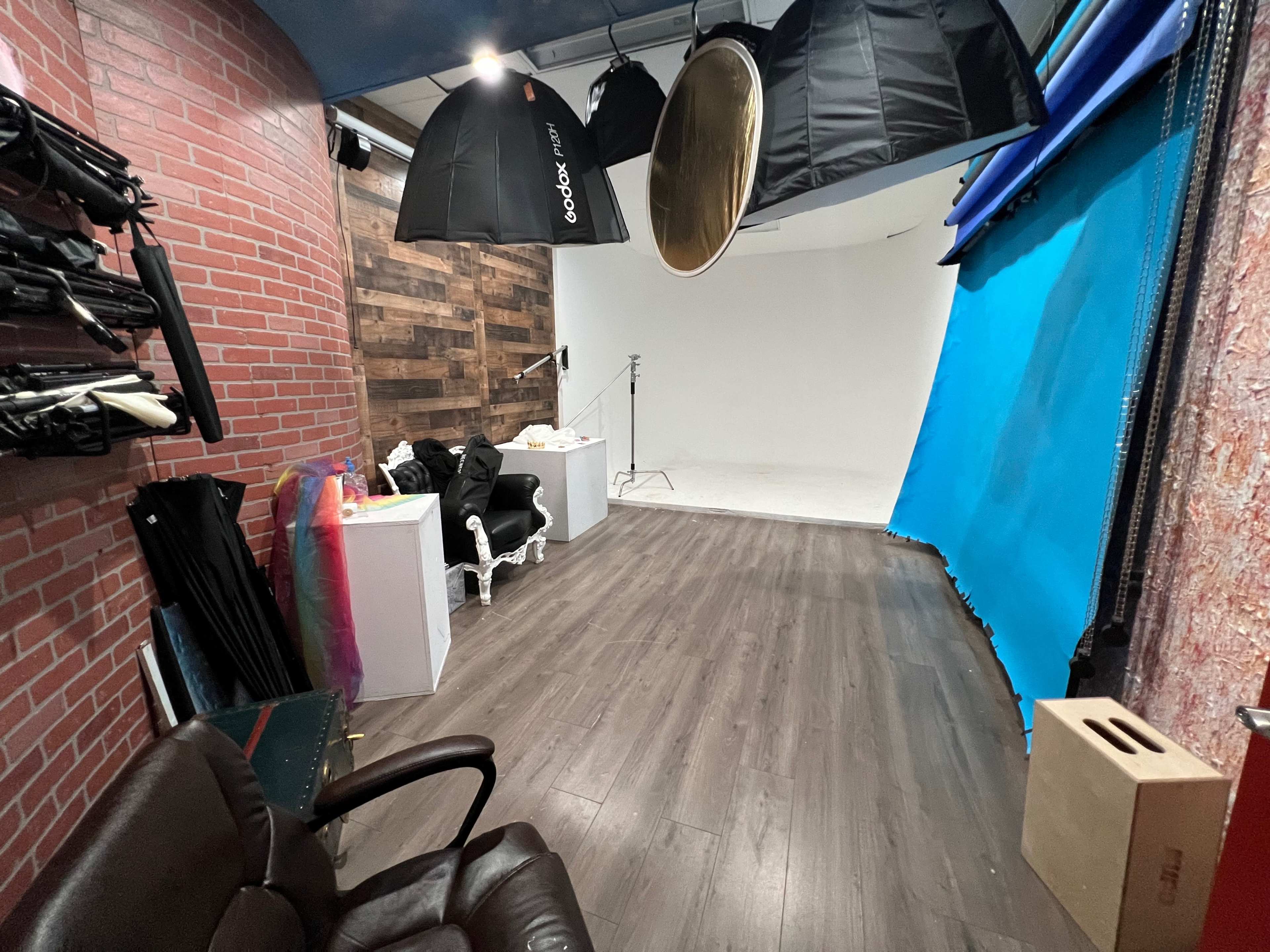 A photography studio with a wooden accent wall, lighting umbrellas hanging from the ceiling, and various props on the floor.
