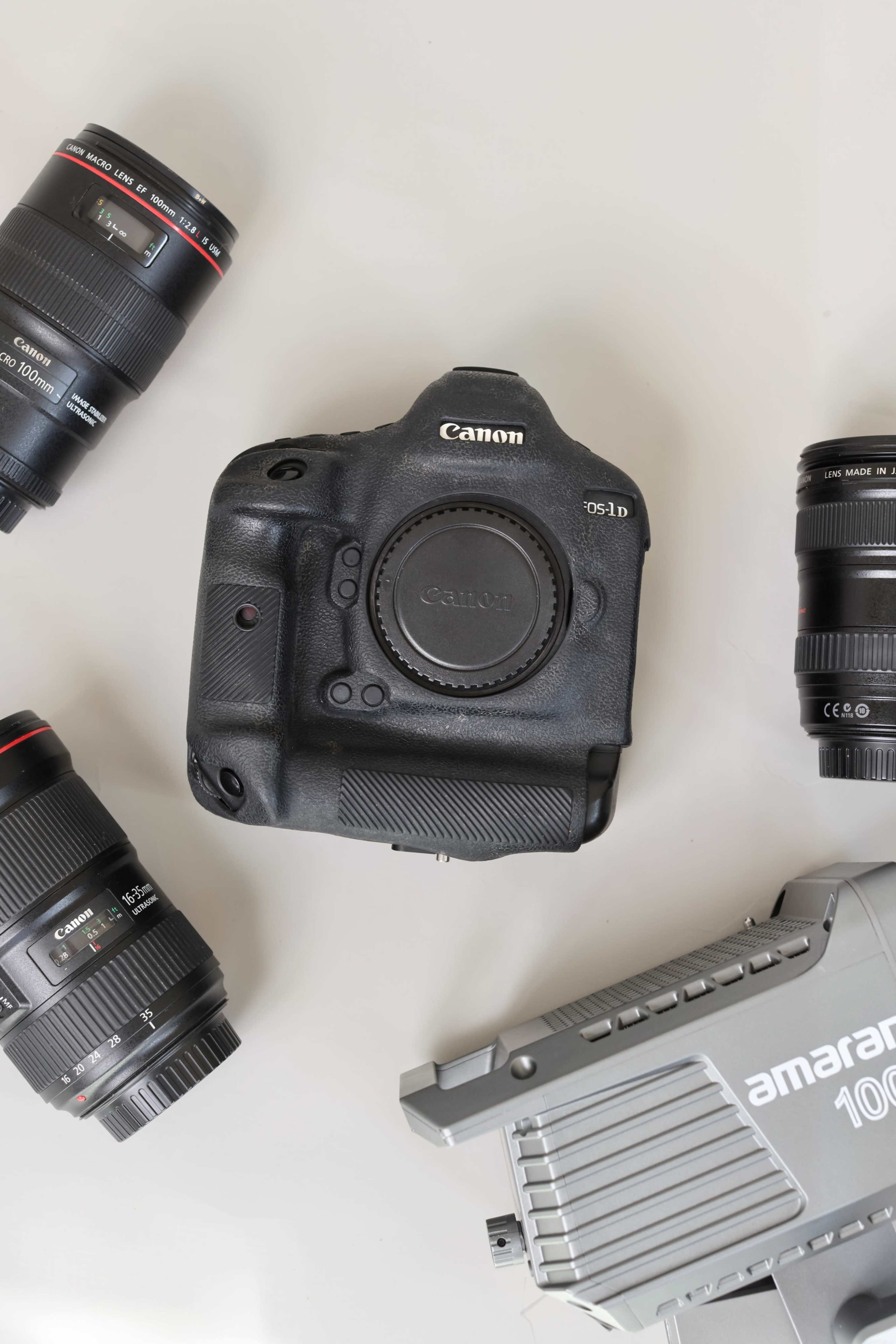 A Canon EOS-1D camera body is centered among four camera lenses and a lighting device.