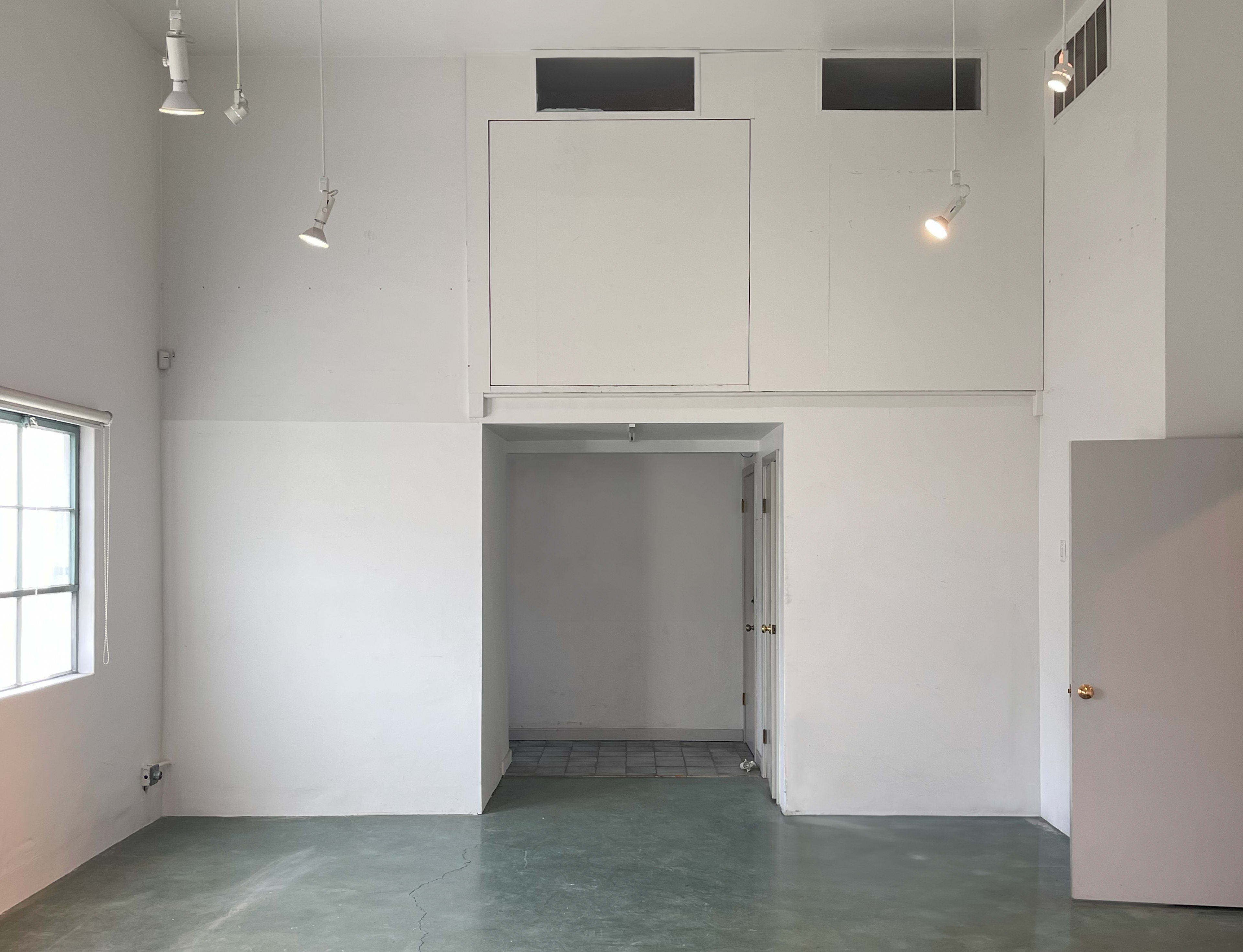 An empty room with white walls, a concrete floor, and a high ceiling featuring spotlights.