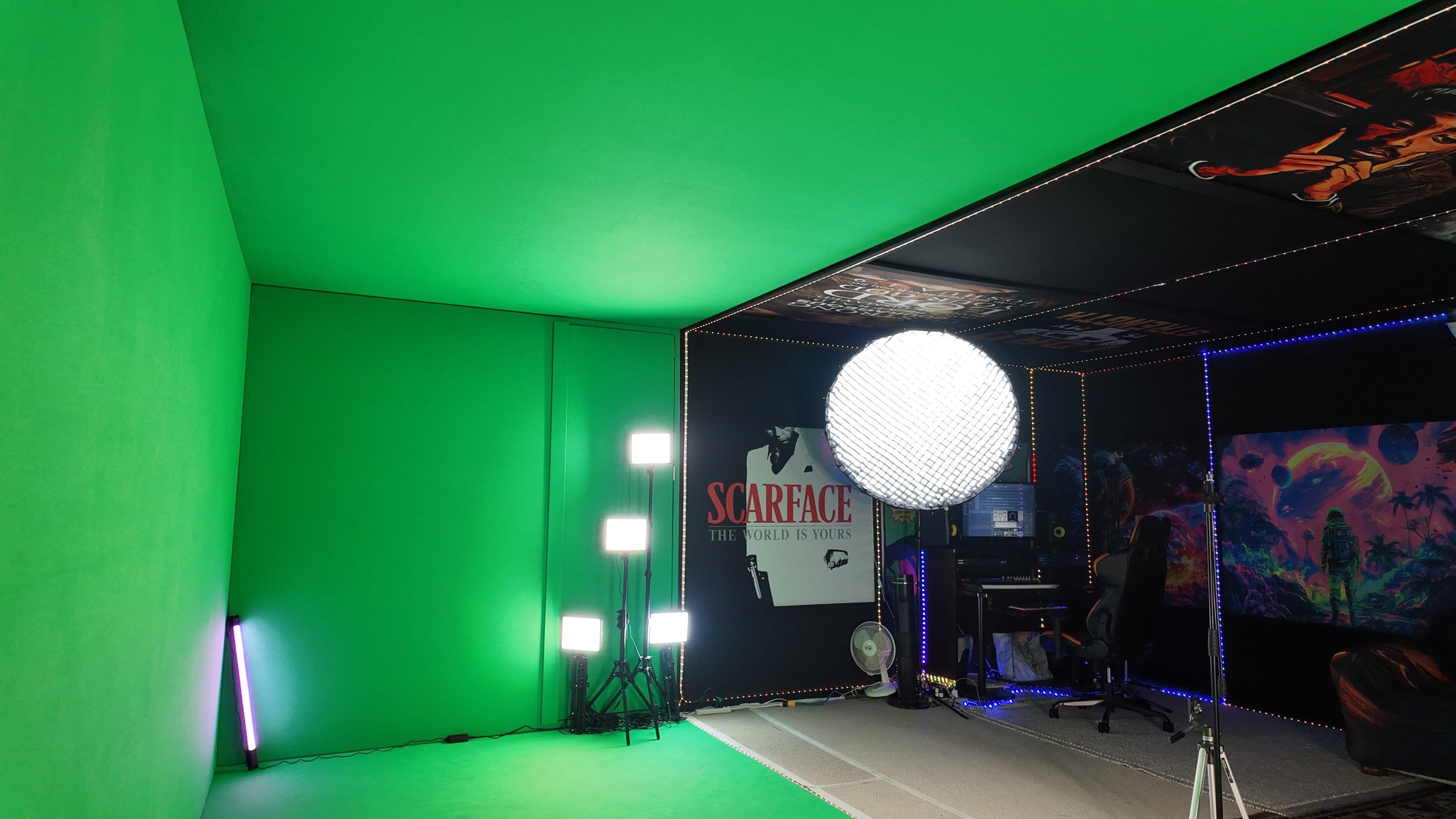 The image shows a green screen studio equipped with lighting, posters on the walls, and a computer workstation in one corner.