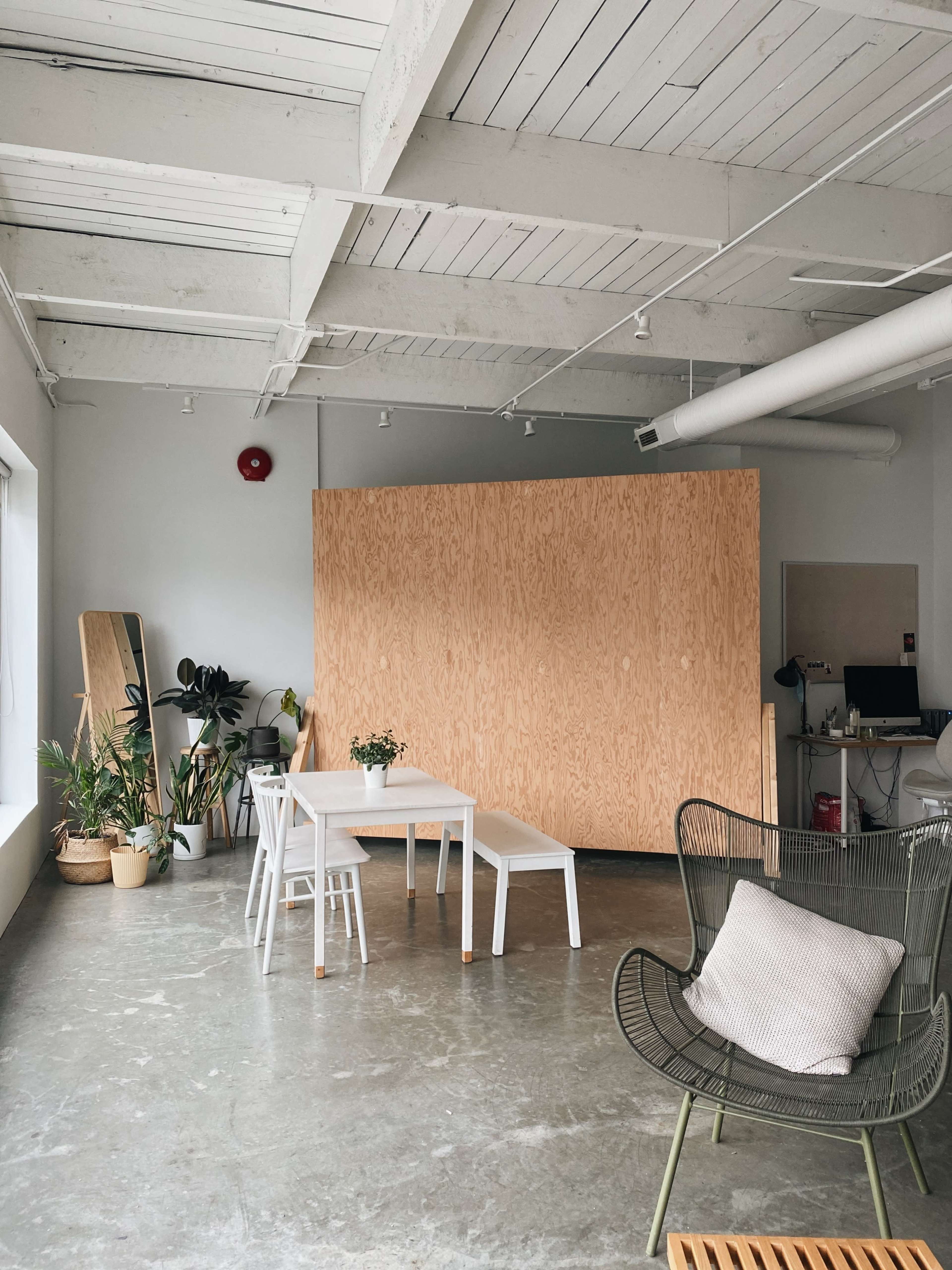 A modern office space with a large wooden partition, a dining table with chairs, and various plants in pots.