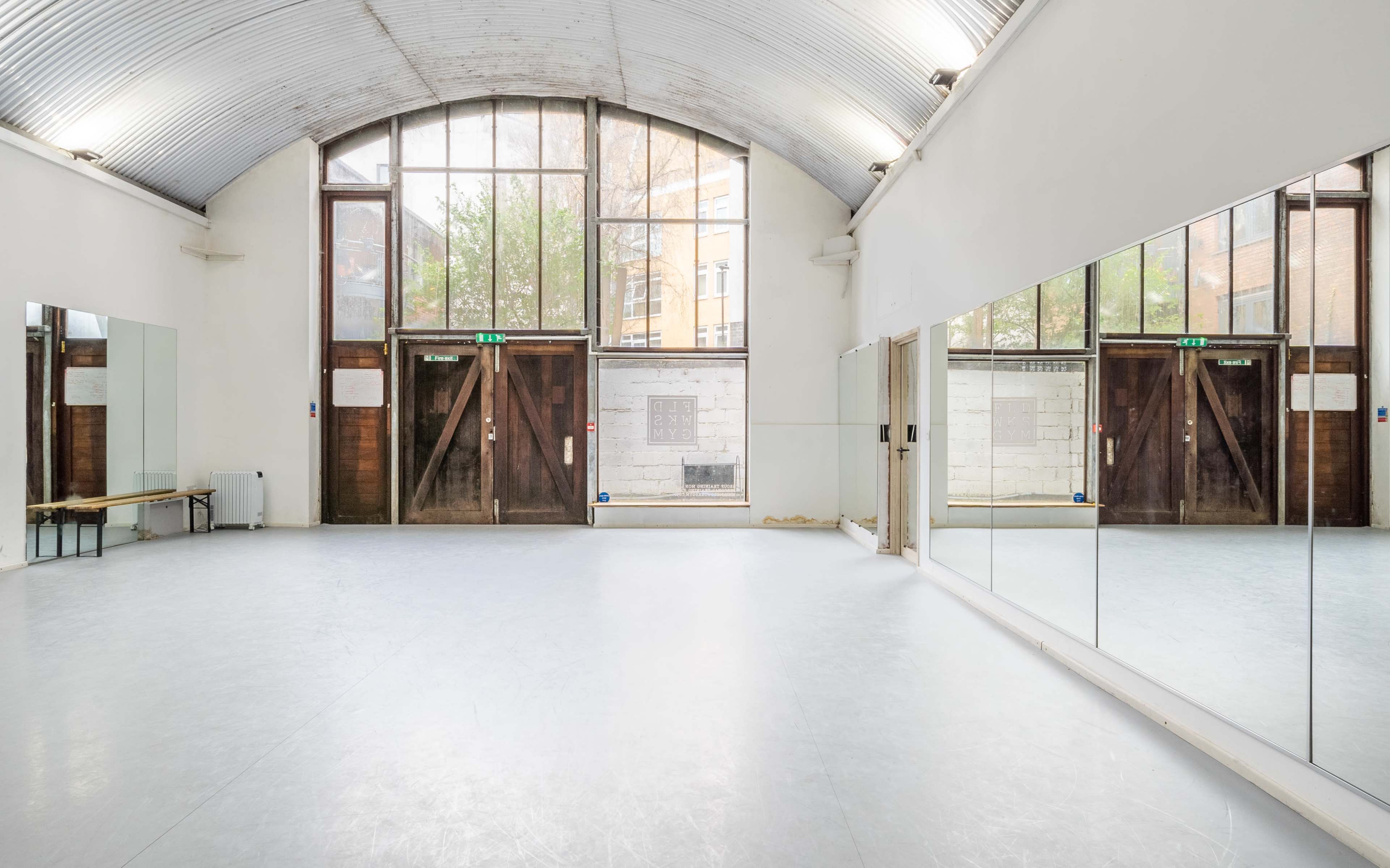 A spacious dance studio featuring large mirrors along one wall and tall windows allowing natural light to enter.