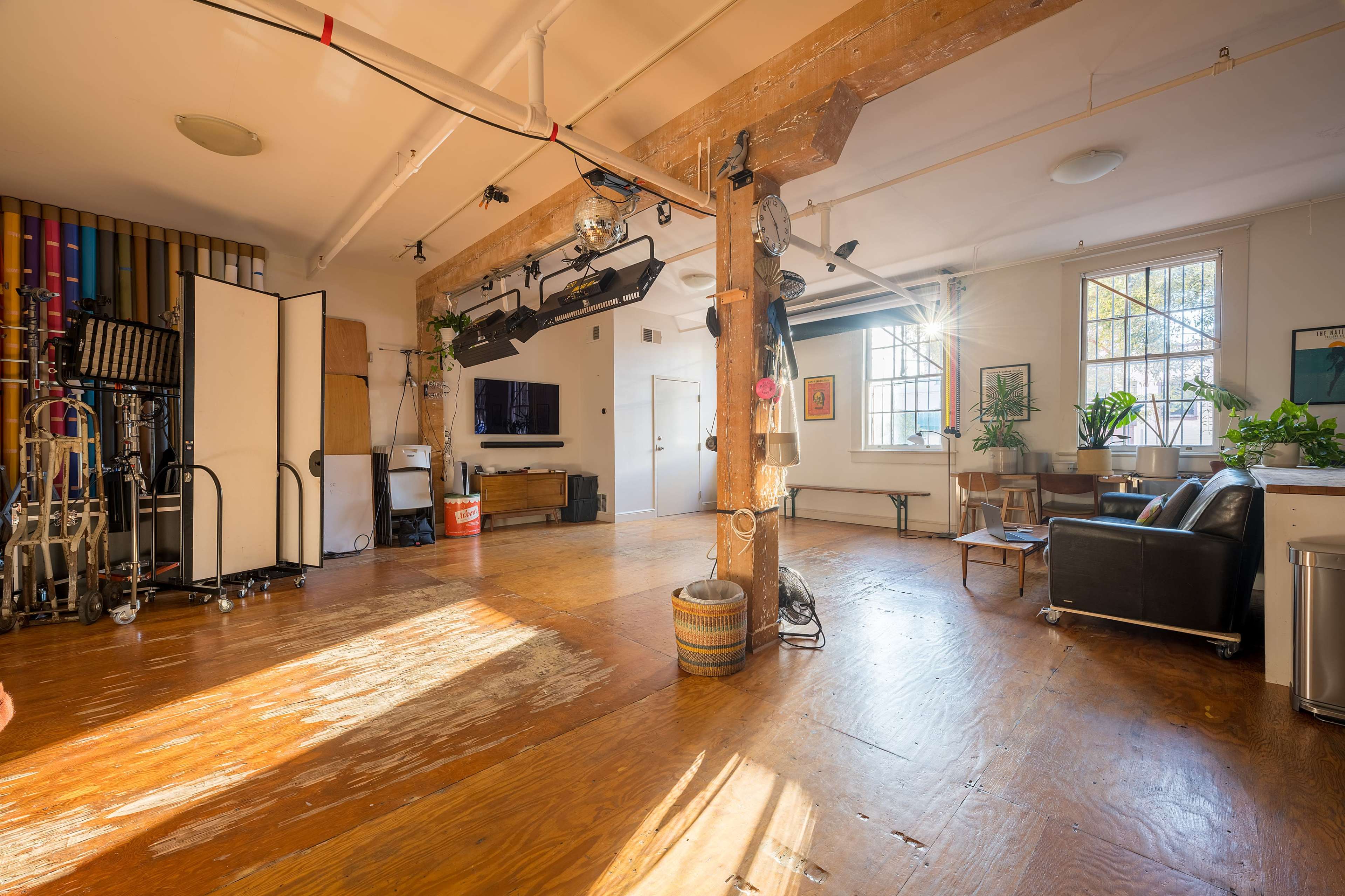 A spacious, well-lit studio interior with wooden floors, large windows, and various furniture and equipment arranged throughout the space.