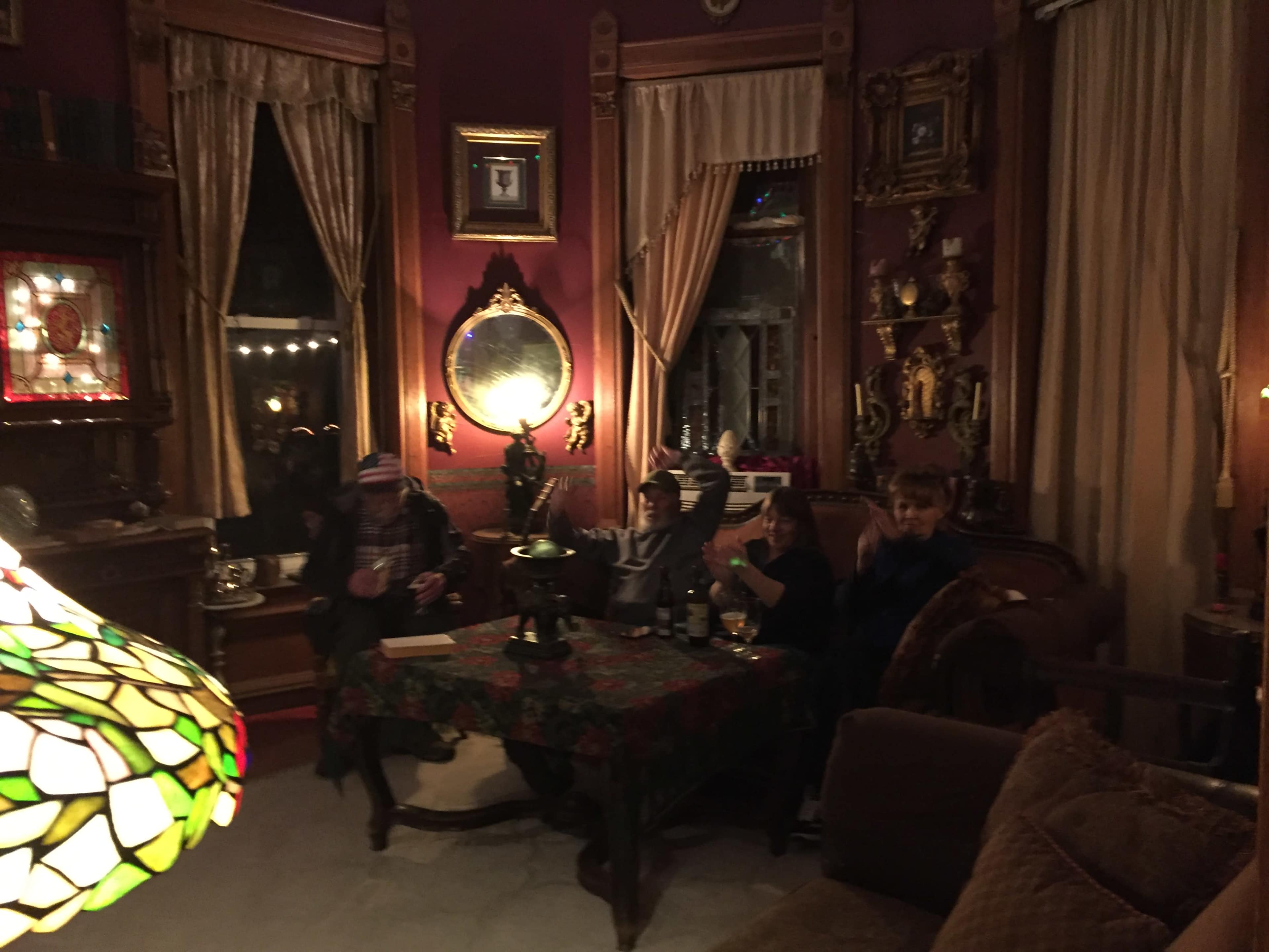 The image shows three people sitting on a couch in a richly decorated room with ornate furnishings and warm lighting.
