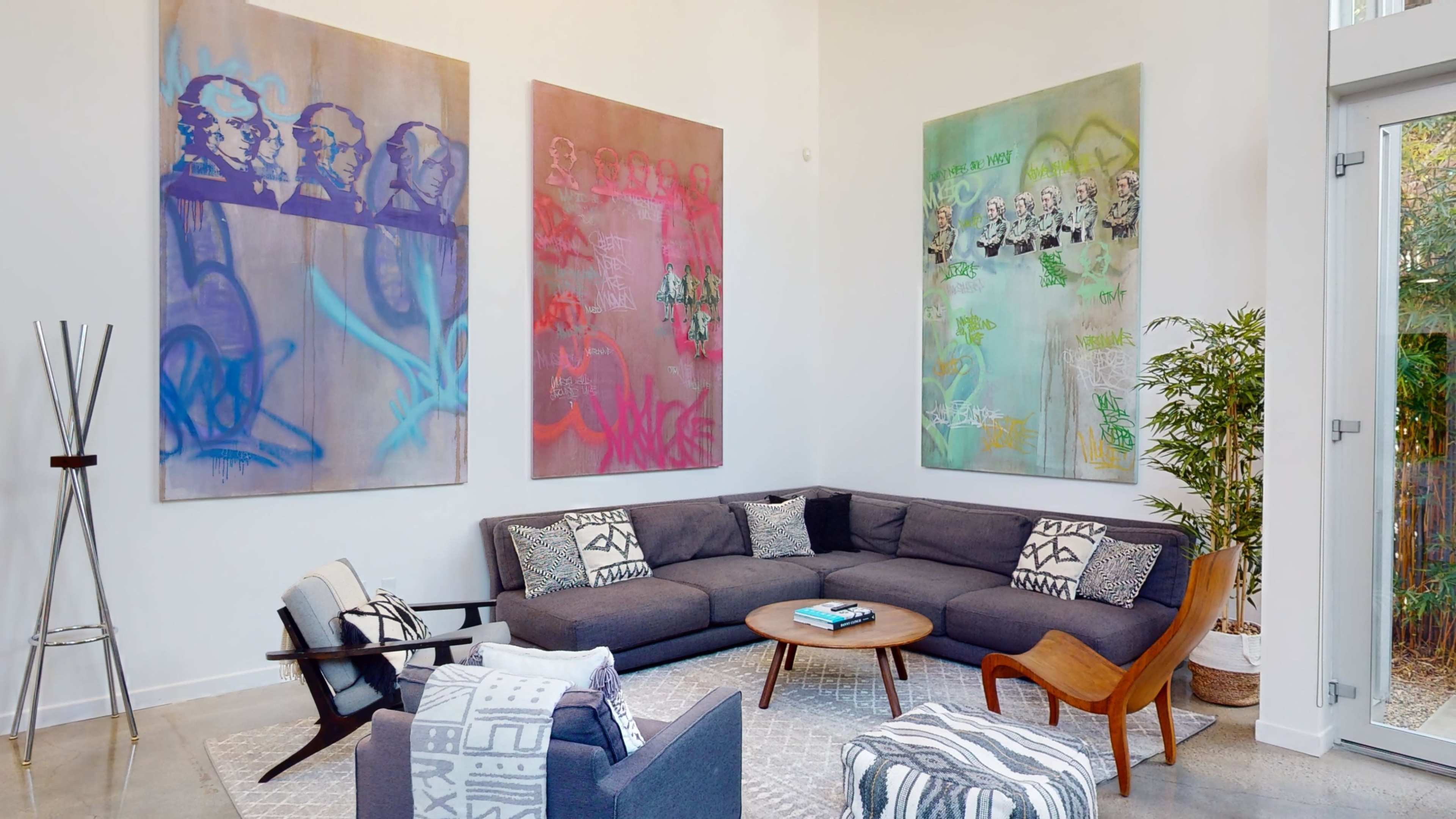 The scene features a modern living room with a sectional sofa, a coffee table, and three large abstract paintings on the wall.