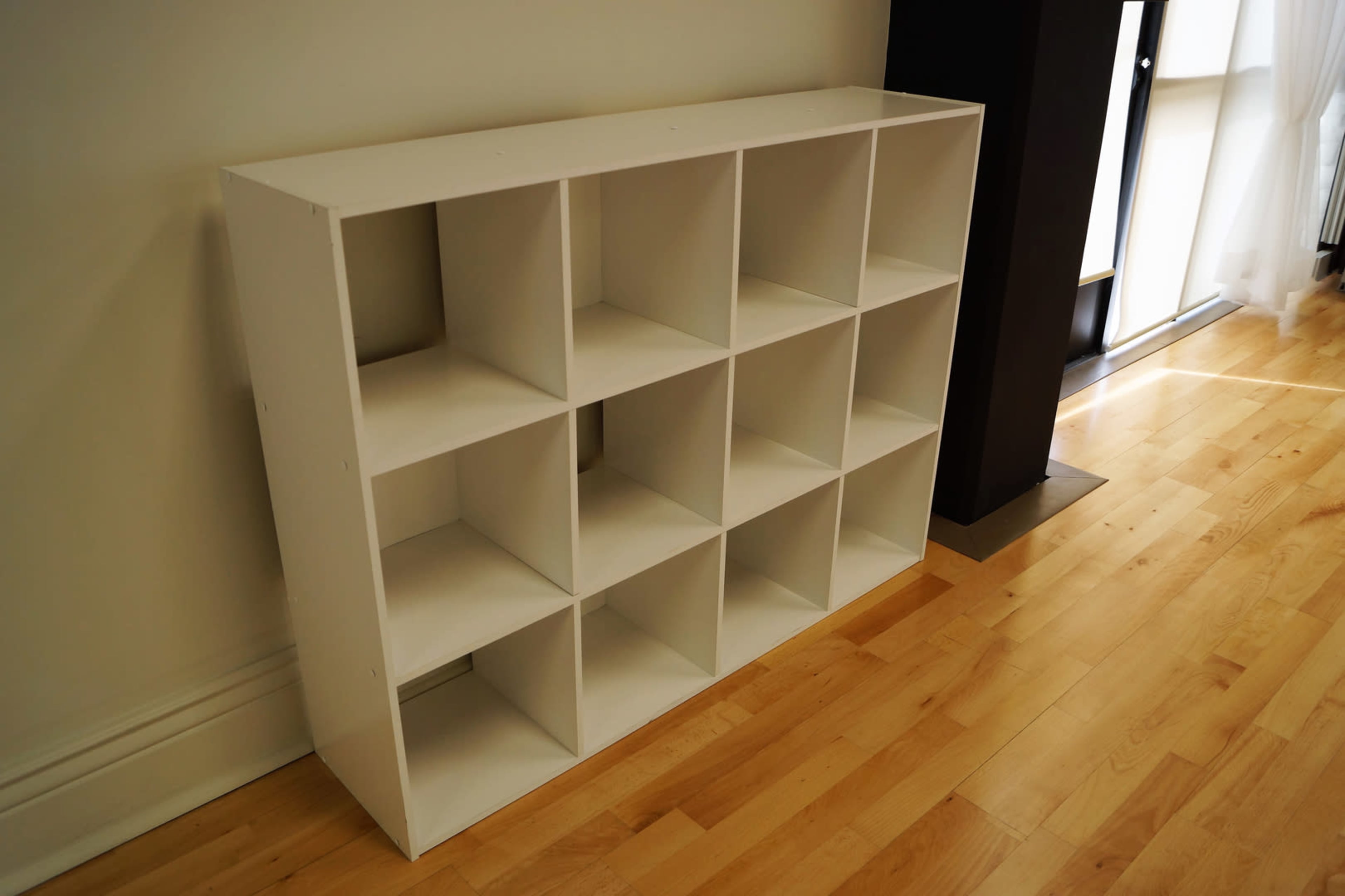 A white shelving unit with twelve square compartments positioned against a wall on a hardwood floor.