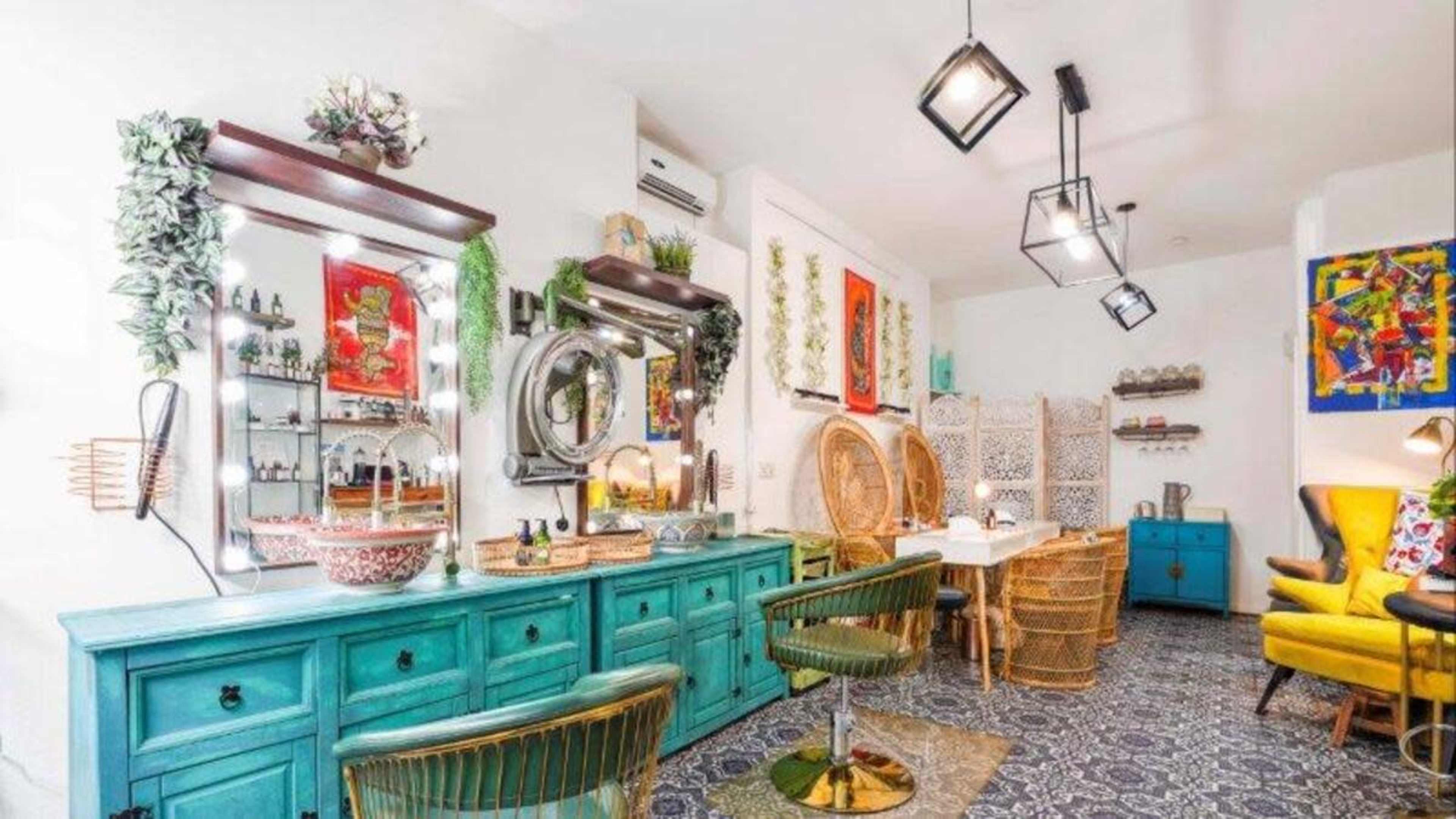 A brightly lit café with turquoise furniture, decorative mirrors, and plants, featuring a mix of rattan chairs and a dining table.