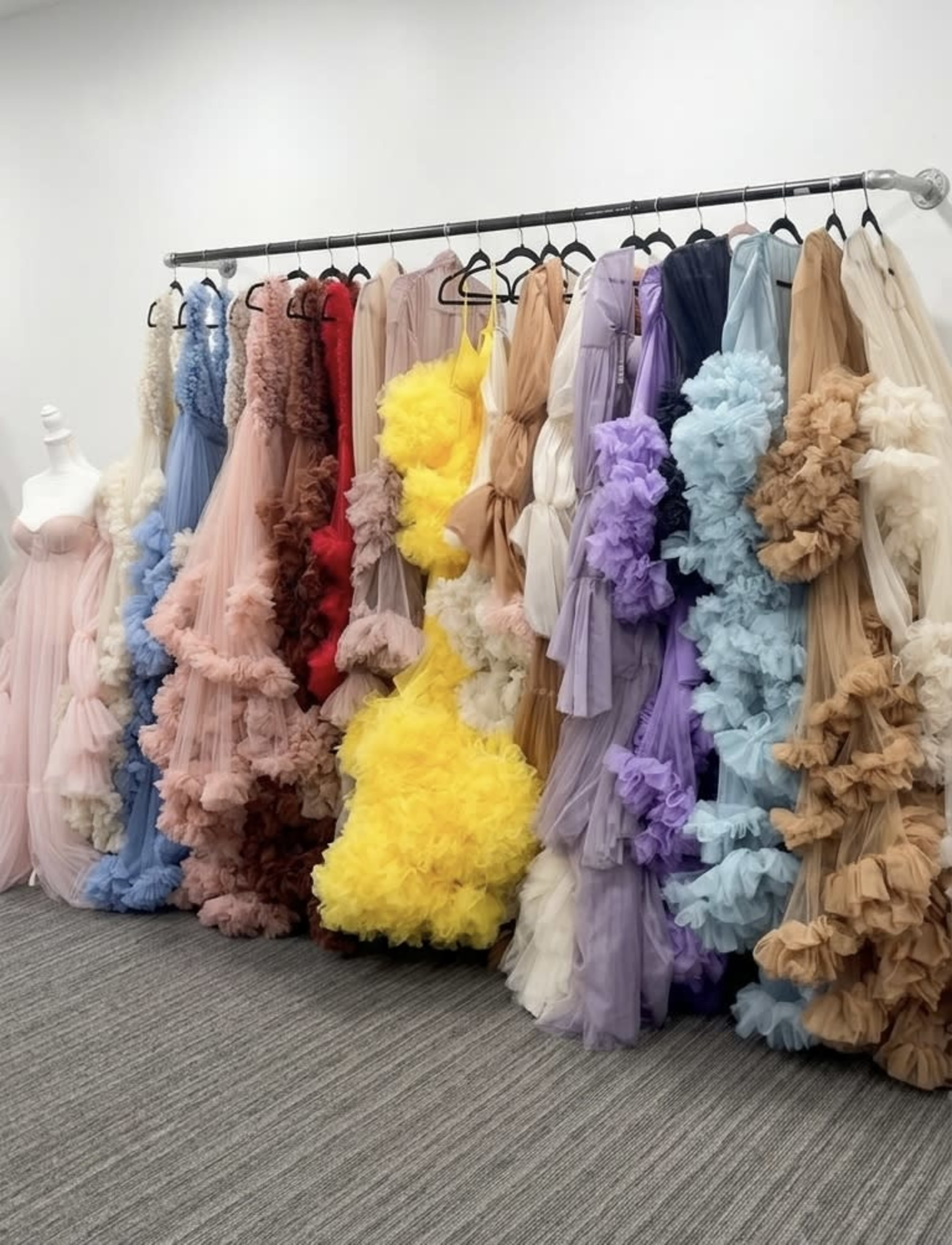 A rack displays a variety of colorful, ruffled dresses hanging in a row.