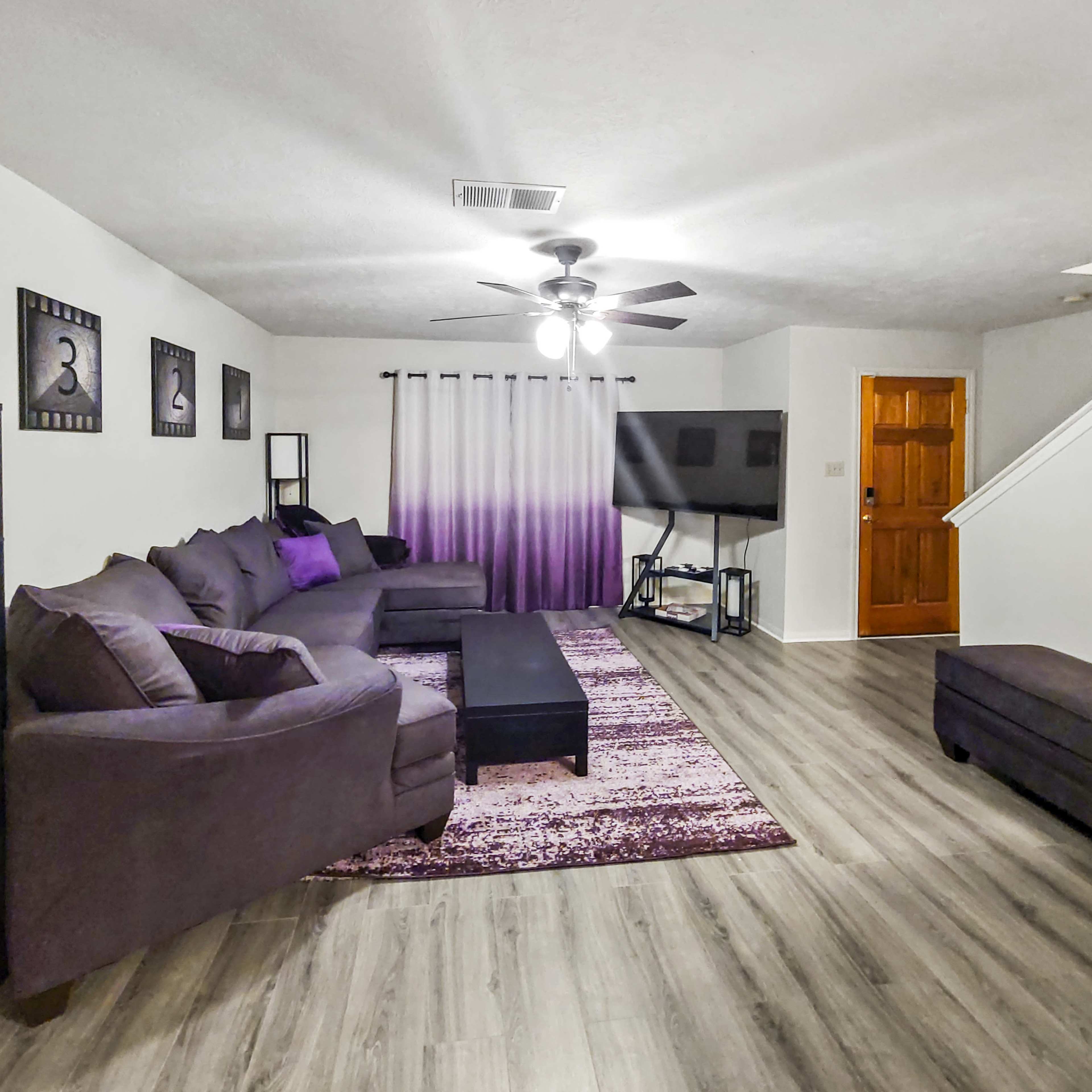 The living room features a sectional couch, a coffee table, and a television stand against a gradient curtain backdrop.