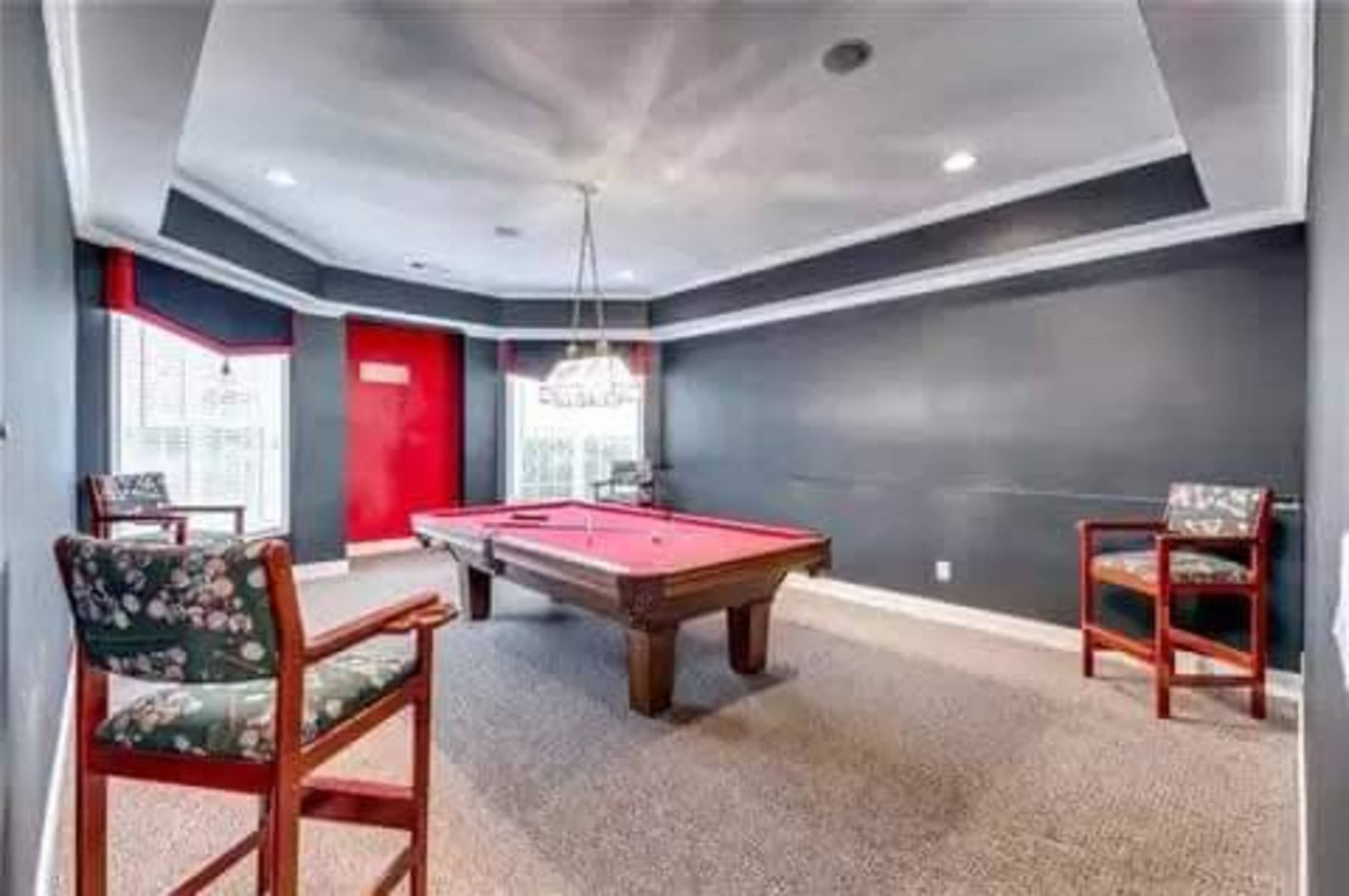 A well-lit game room featuring a pool table surrounded by two upholstered chairs.