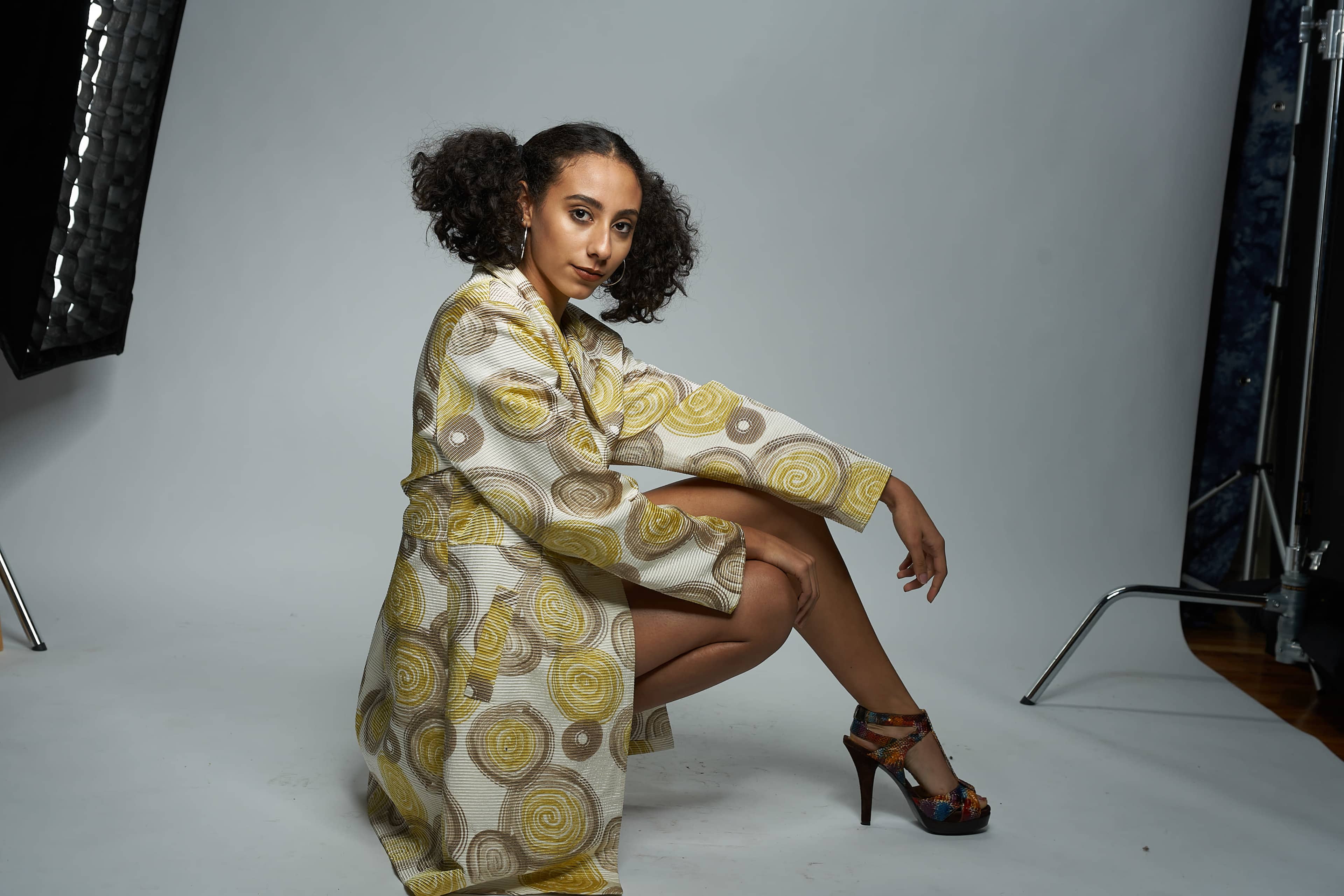 A model poses on a studio set, wearing a patterned robe and high-heeled shoes.